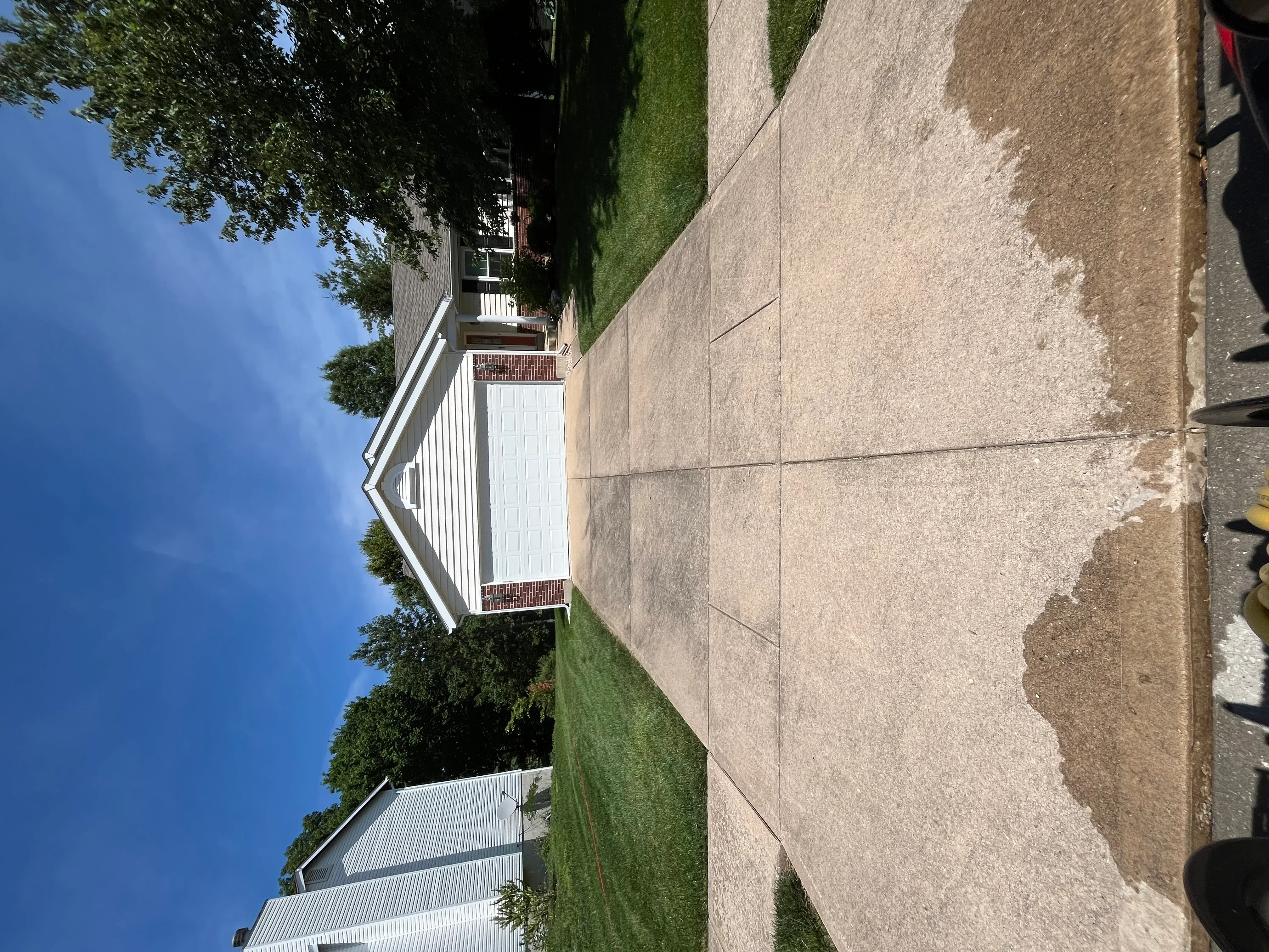 Clean concrete driveway and walkway with white trim house and green lawn