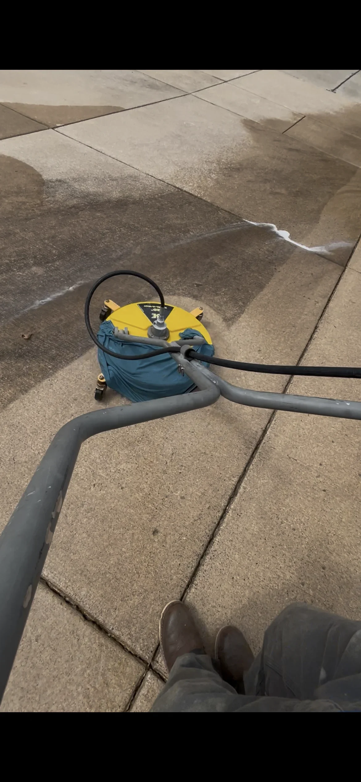 Yellow and blue pressure washer cleaning concrete patio pavers with visible water stream