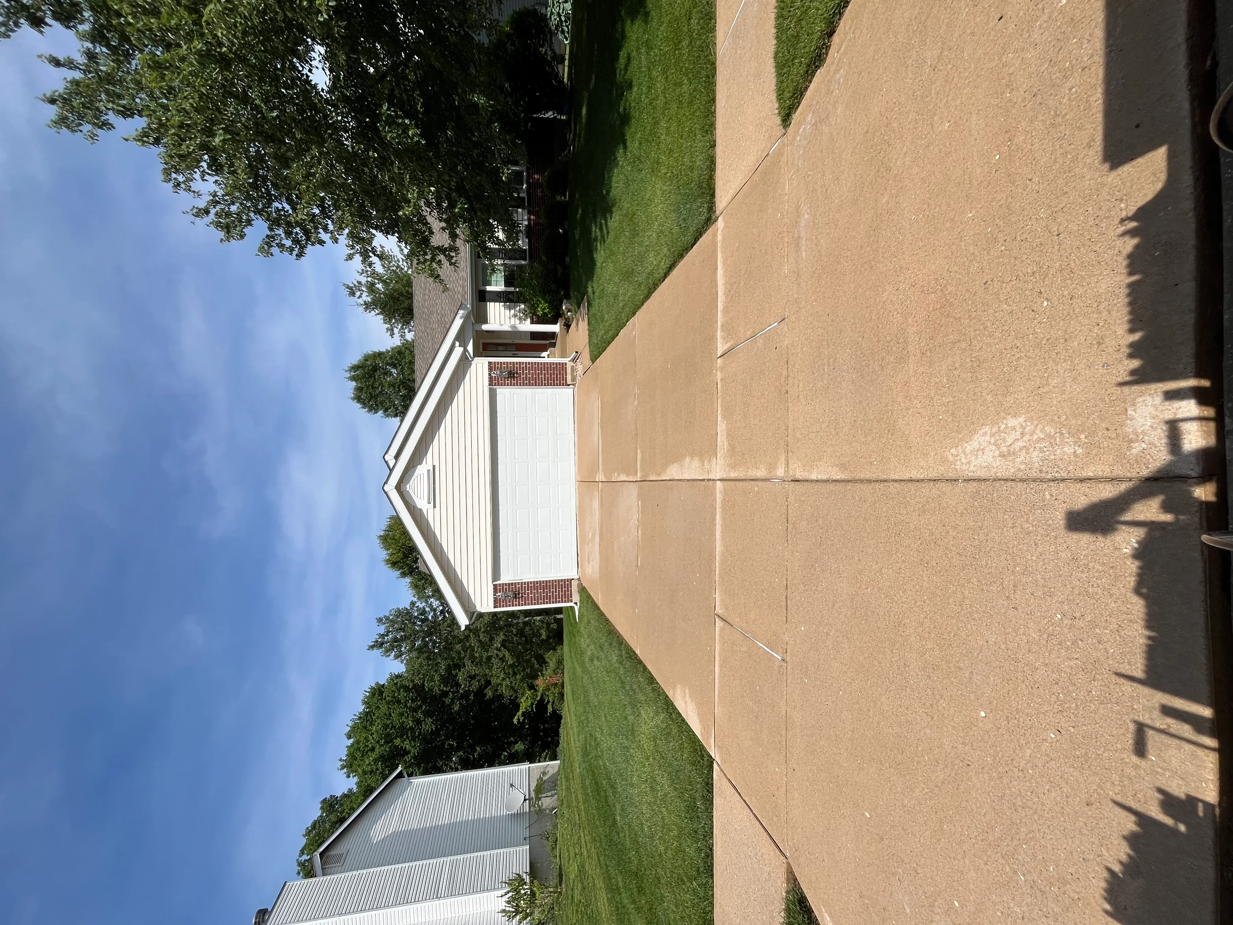 Clean concrete driveway with white-trimmed house and green lawn