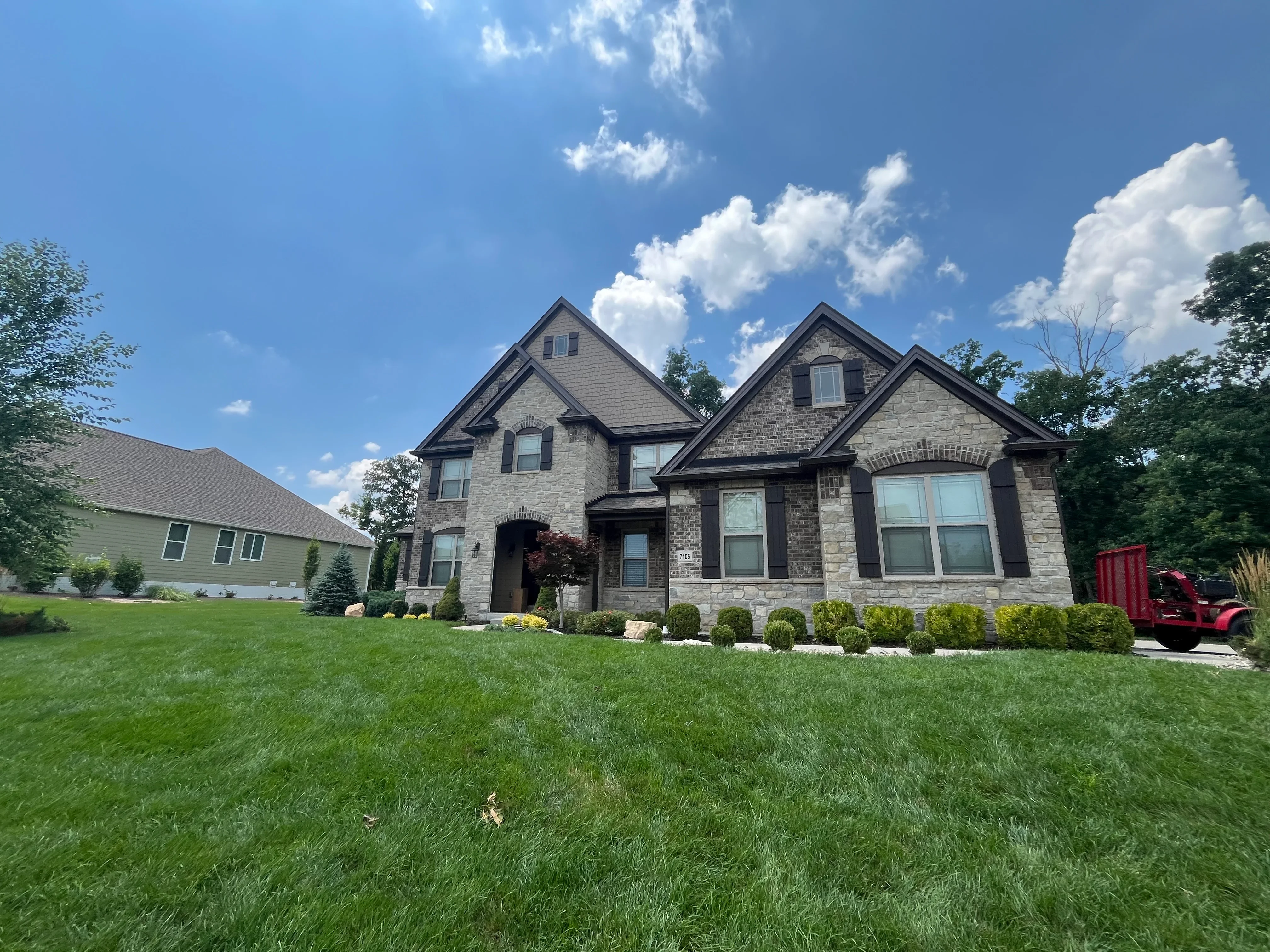 Two-story stone home with dark roof, gabled peaks, and manicured landscaping in Wentzville