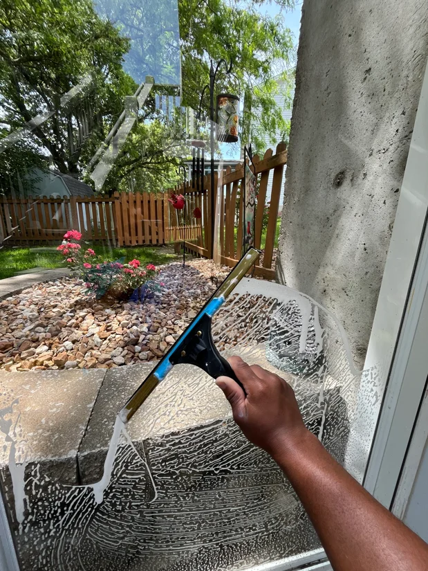 Soft washing concrete patio and foundation wall with specialized equipment near residential landscaping