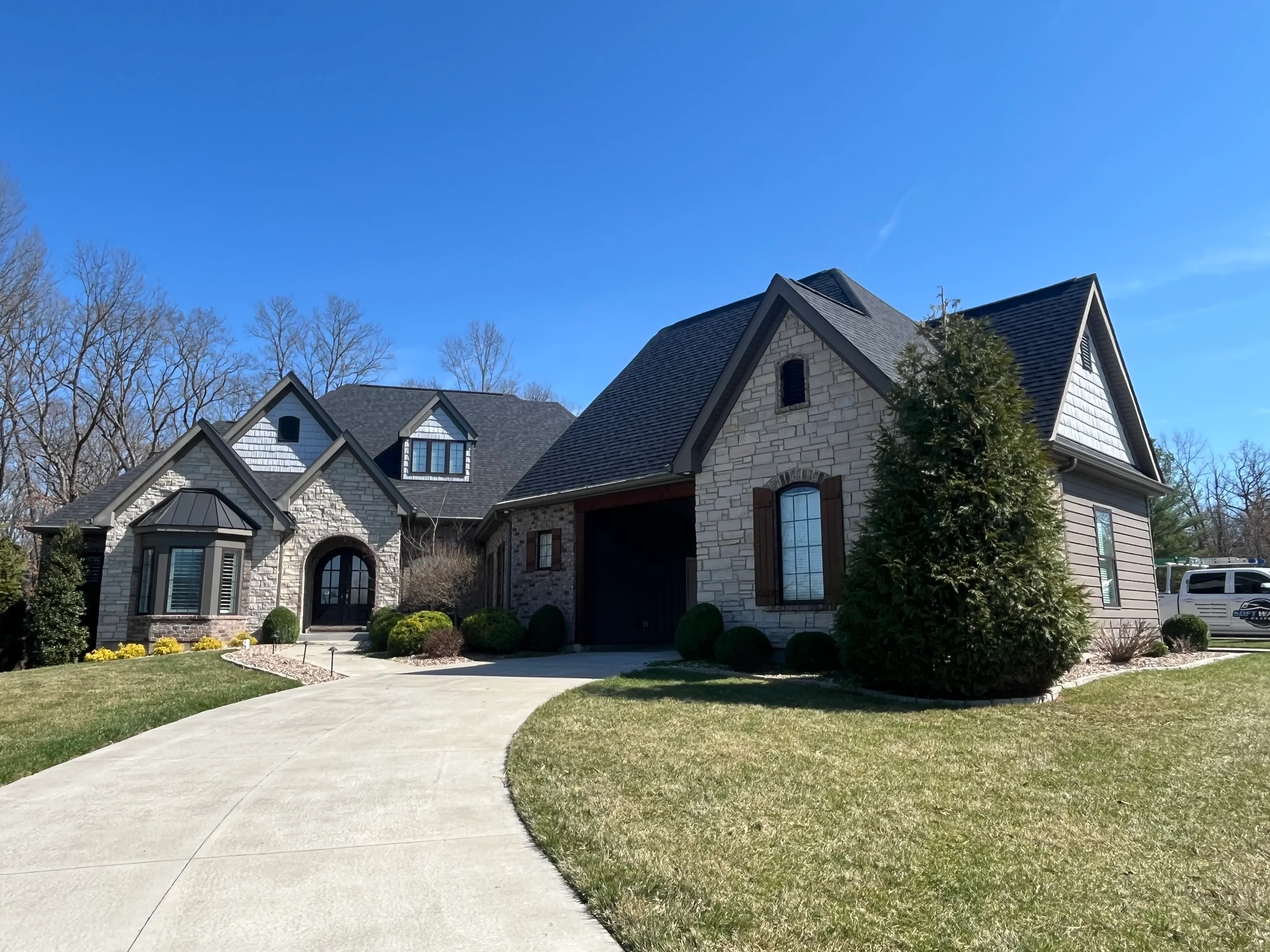 Clean stone and siding home with freshly washed driveway and manicured lawn