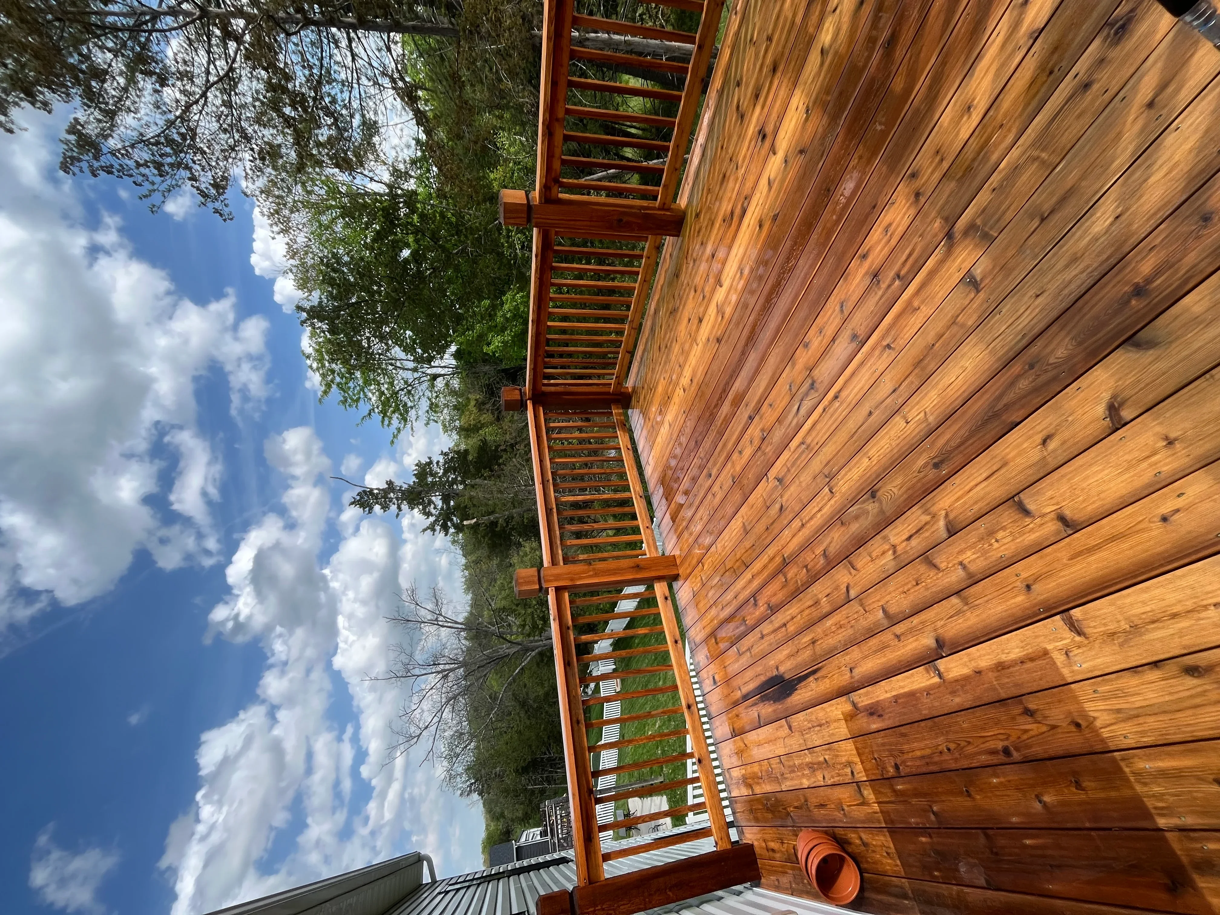 Clean wooden deck and siding with metal railings and green landscaping
