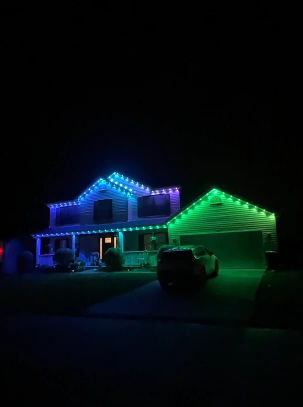 LED holiday lights in blue, green, and purple outlining residential home roofline at night