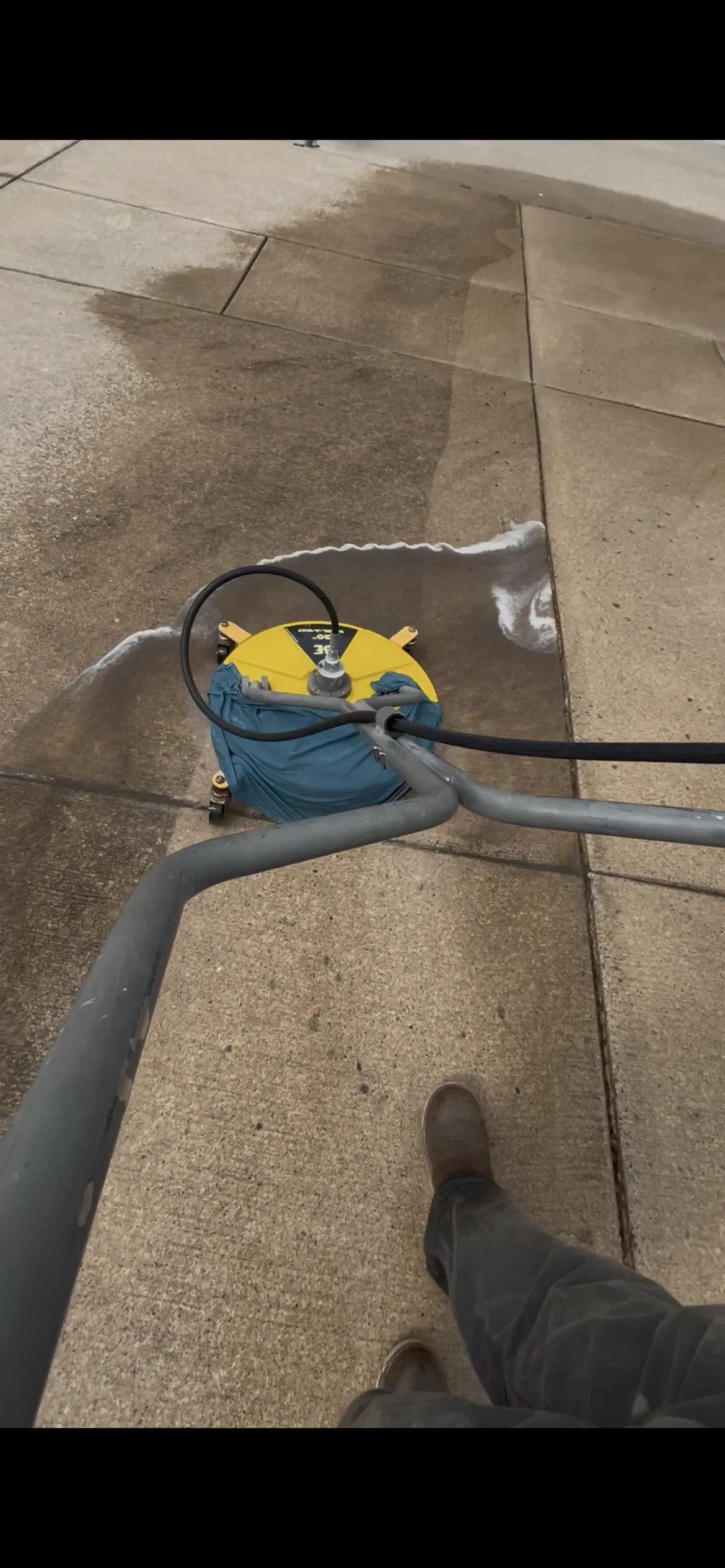 Pressure washing concrete patio with yellow and blue equipment, showing cleaned versus dirty sections