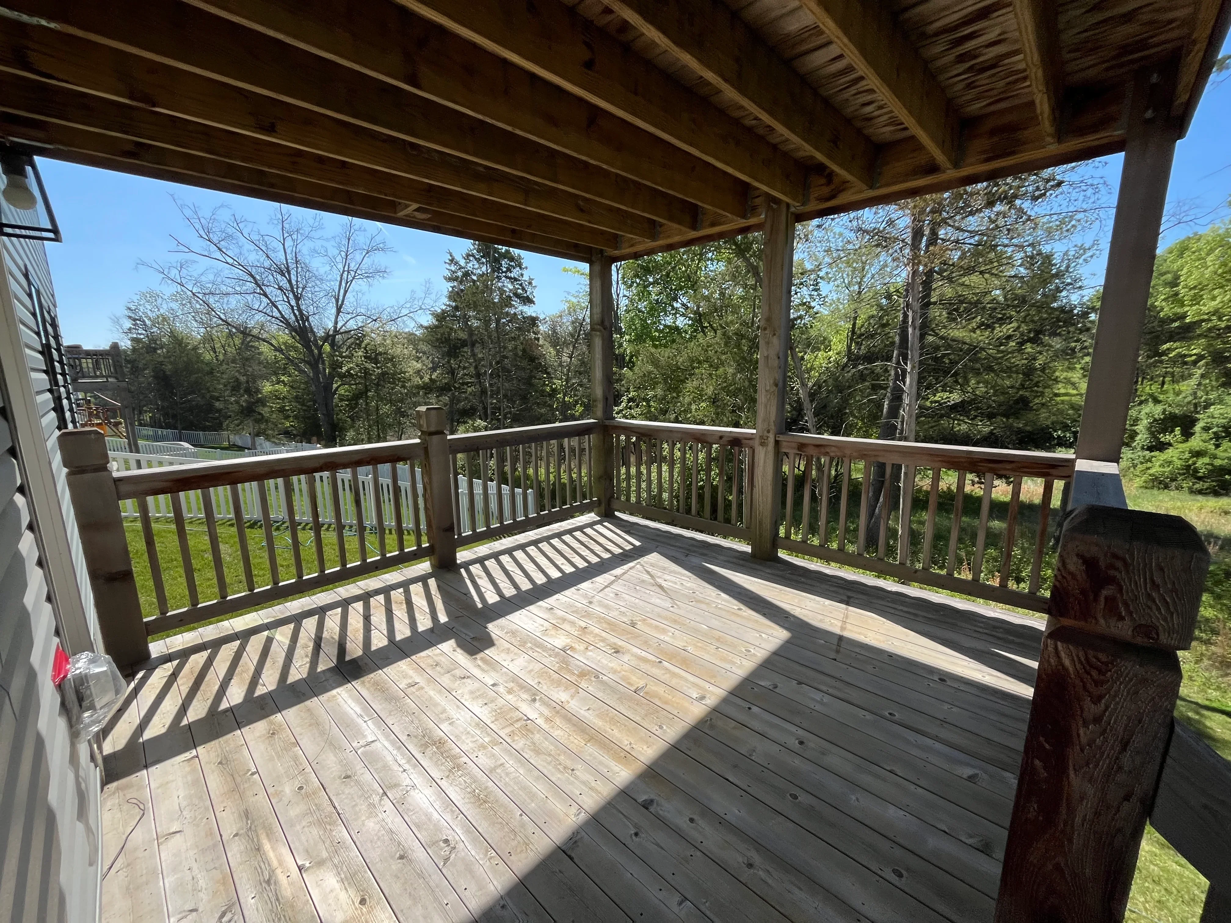 Clean covered deck with wooden railings overlooking wooded yard
