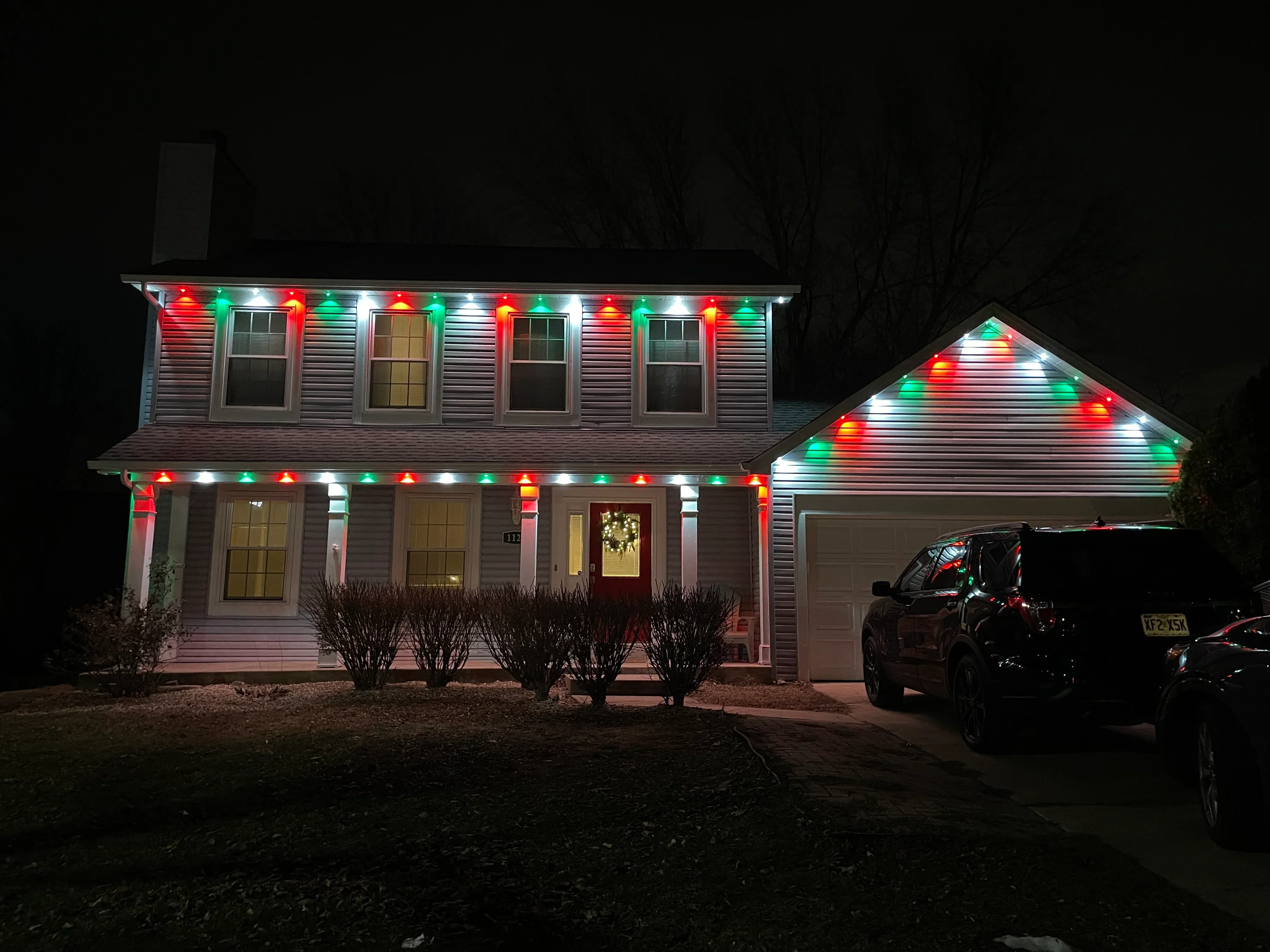 Two-story home with red, green, and white holiday lights installed on roofline and gable at night