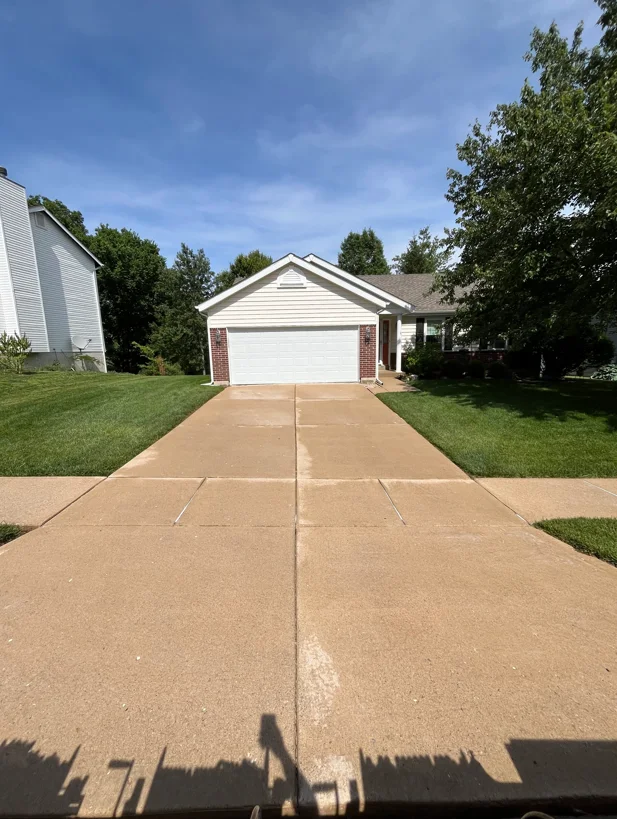Clean concrete driveway with control joints, residential garage and landscaping visible