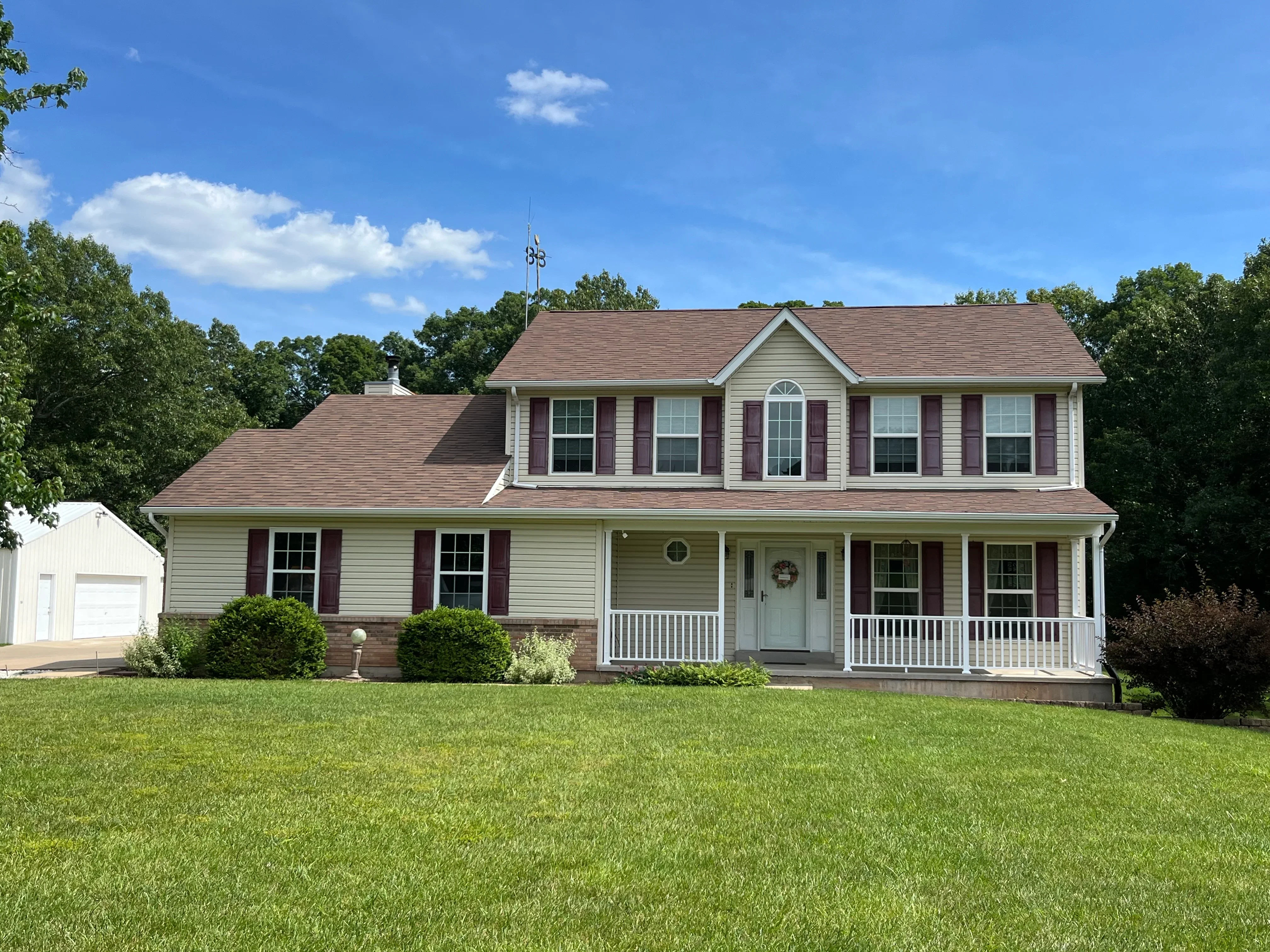 Clean two-story colonial home with white vinyl siding, brick base, and burgundy shutters