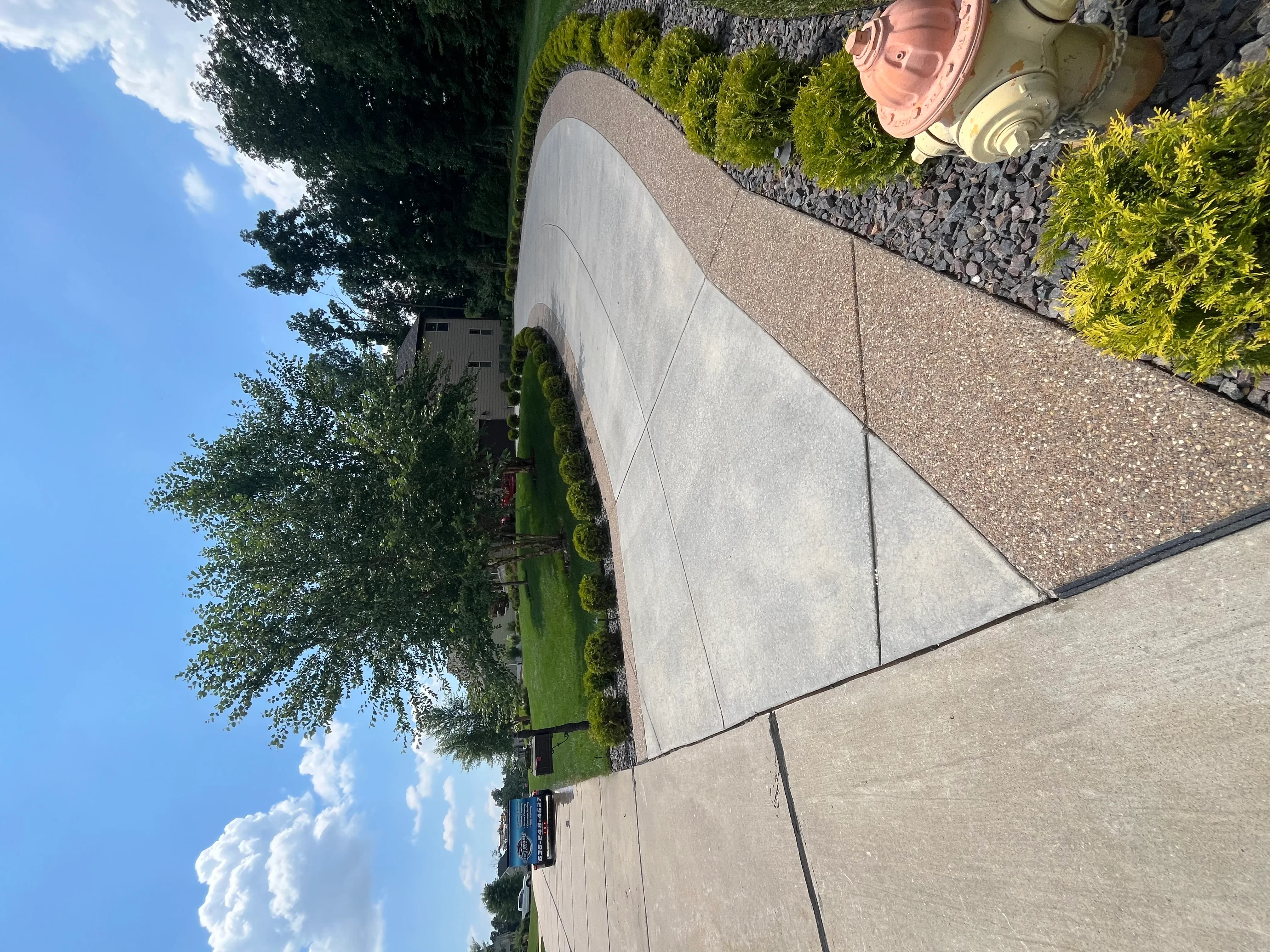 Clean concrete driveway and walkway with landscaping borders and green lawn