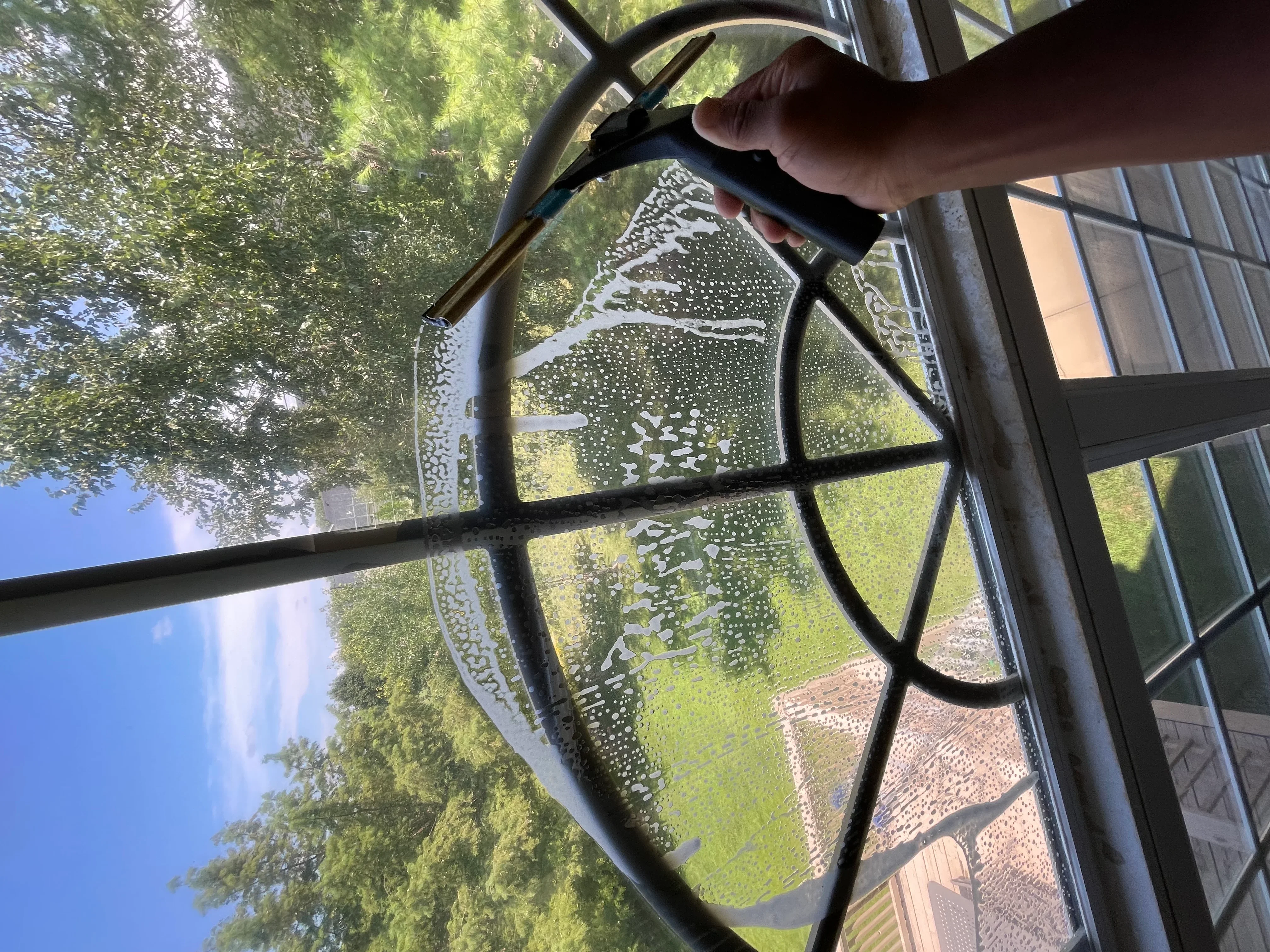 Technician cleaning residential windows with water-fed pole system, revealing lush green yard