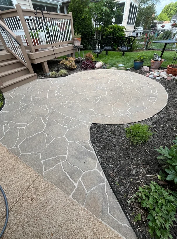 Cleaned flagstone patio with white grout lines, dark mulch beds, and deck stairs