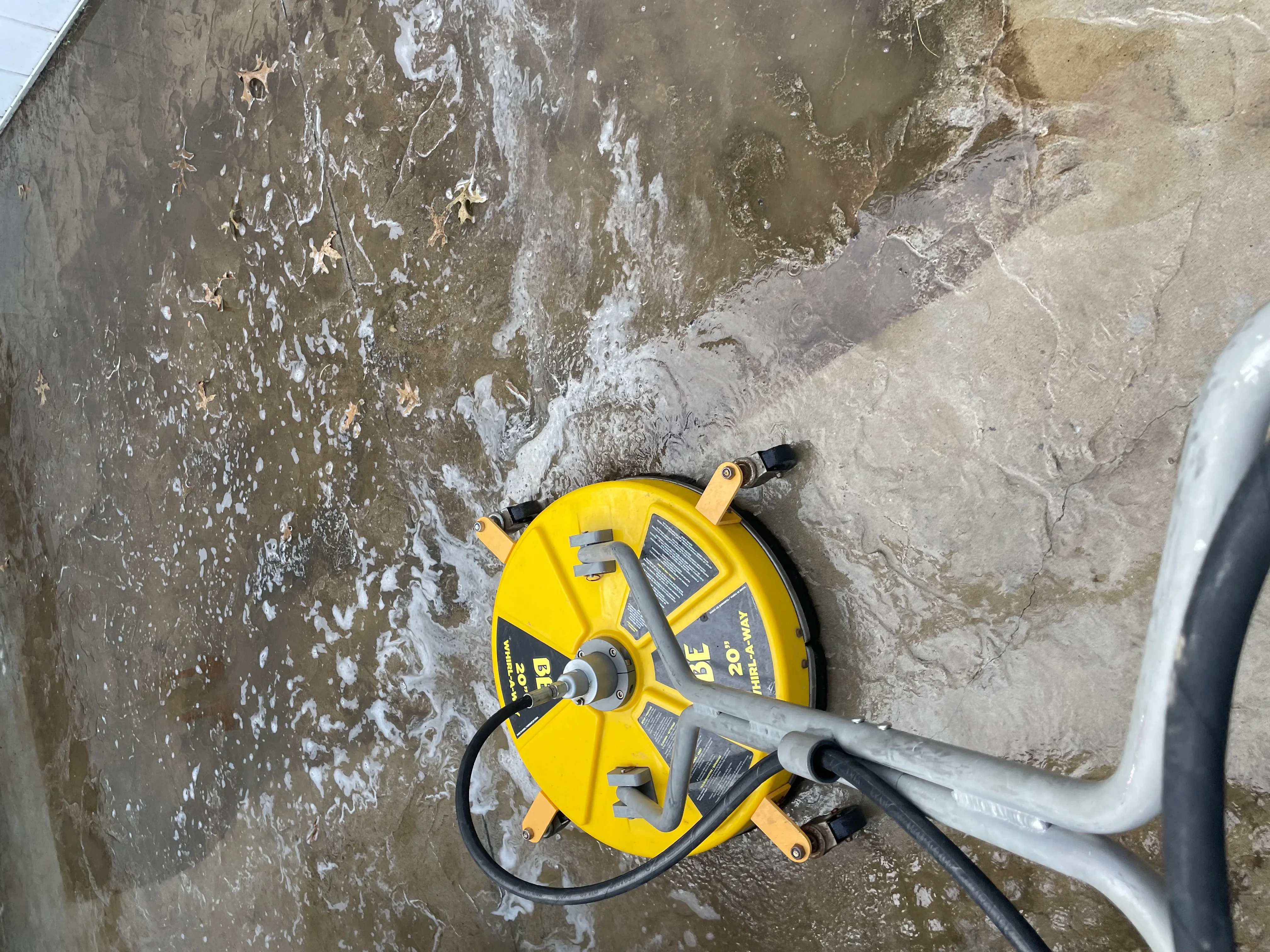 Yellow pressure washer cleaning dirty concrete surface with visible dirt and algae removal