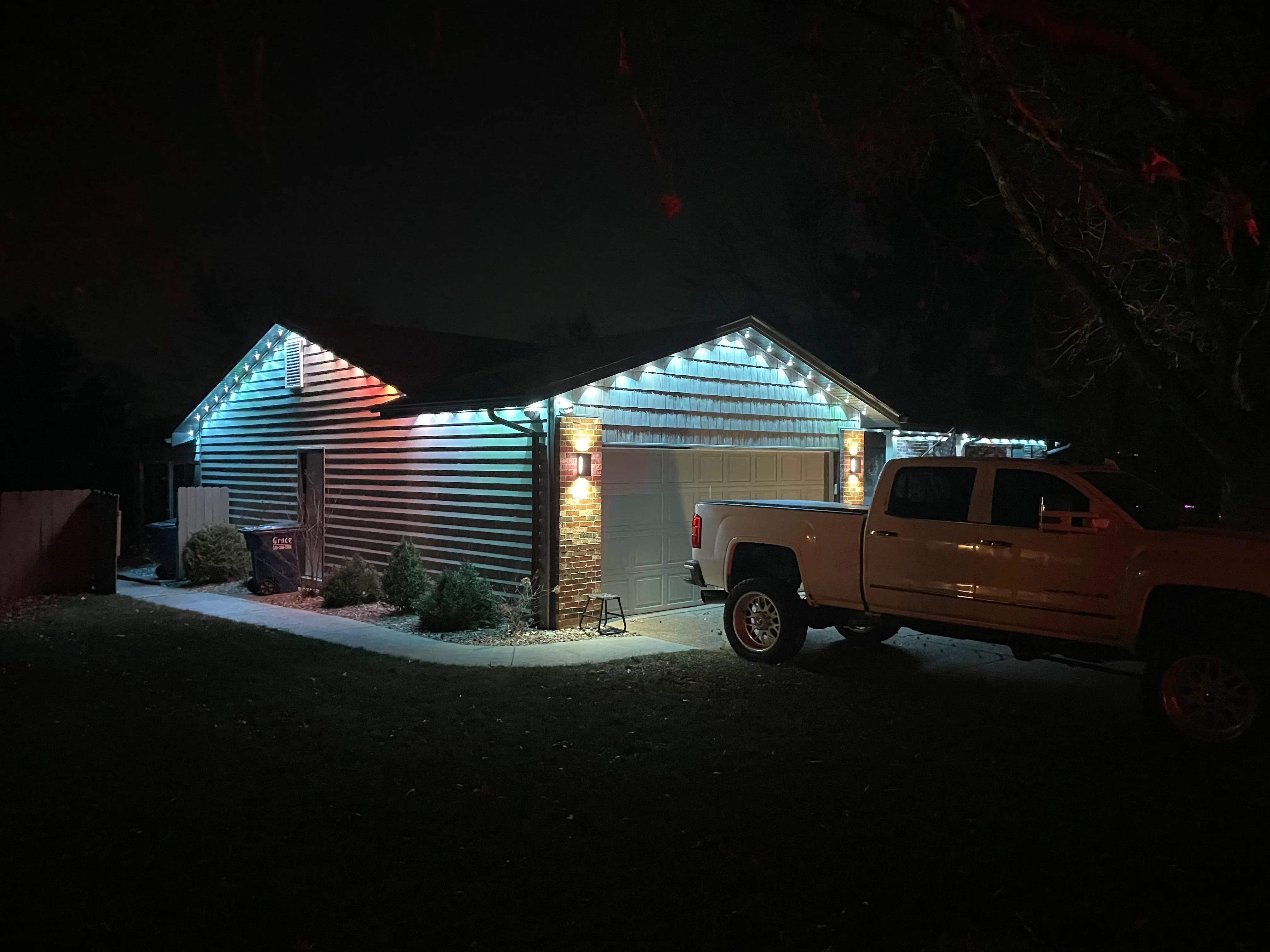Nighttime view of illuminated single-story home with blue and warm white accent lighting on roof and garage