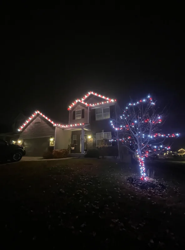 Two-story home with red and white LED lights outlining roofline and blue-red lights wrapped around front tree