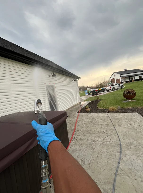 Technician in blue gloves cleaning gutters and downspouts with soft wash equipment on residential home