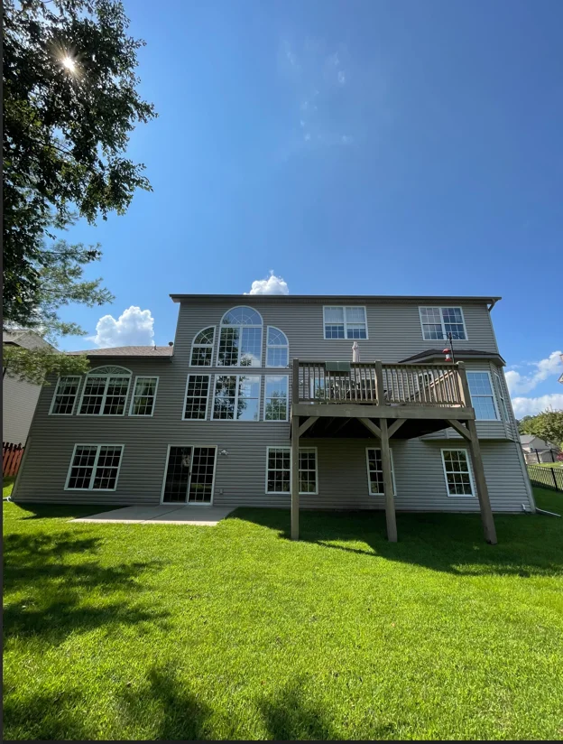 Three-story home with gray vinyl siding, arched windows, and elevated deck after soft wash cleaning