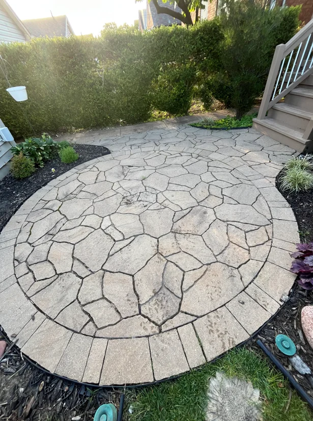 Cleaned flagstone patio with geometric pattern, black mulch beds, and green hedges