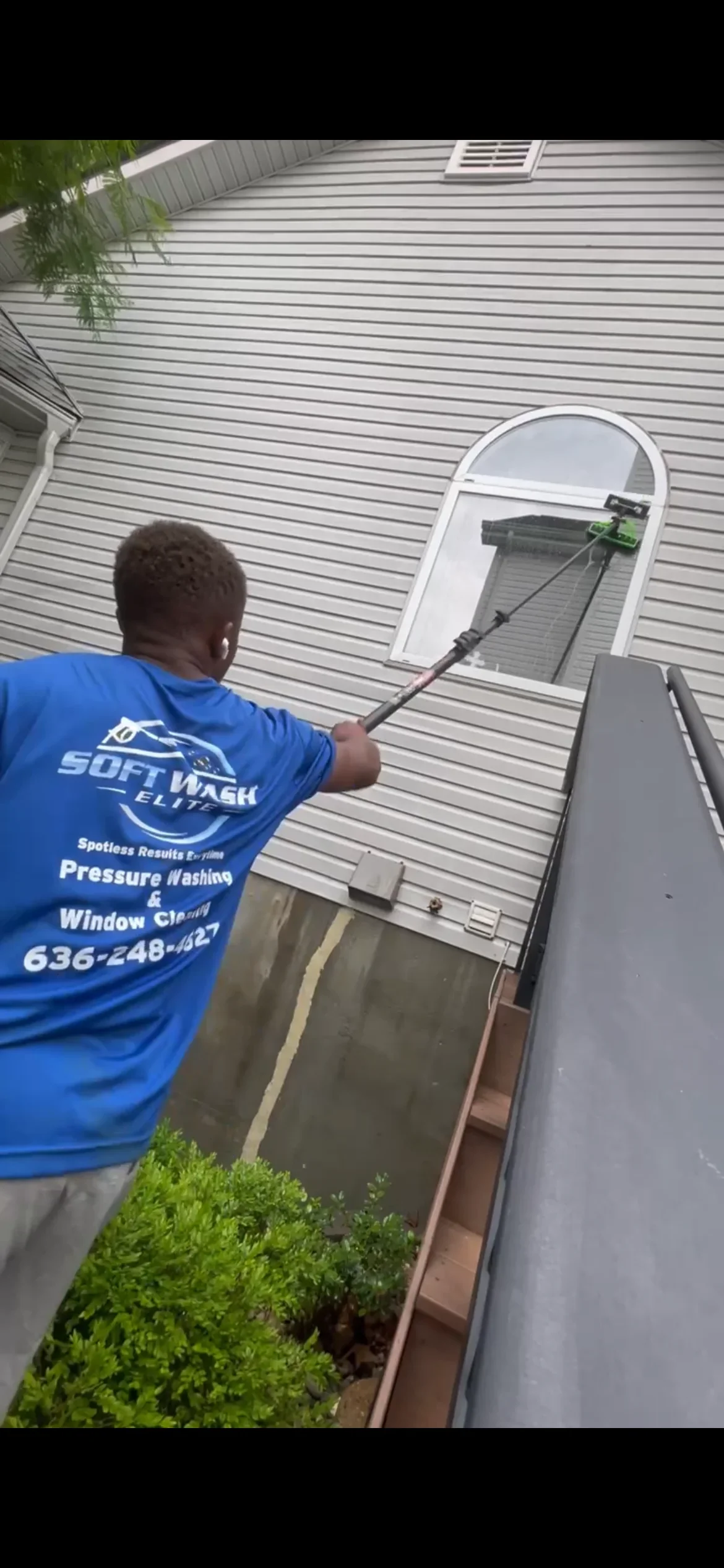 Technician soft washing gutters and soffit on residential home with horizontal siding