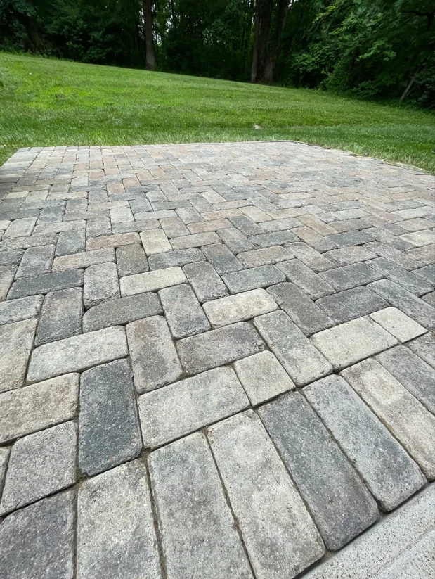 Herringbone paver patio cleaned to reveal gray and tan stone colors with manicured lawn beyond