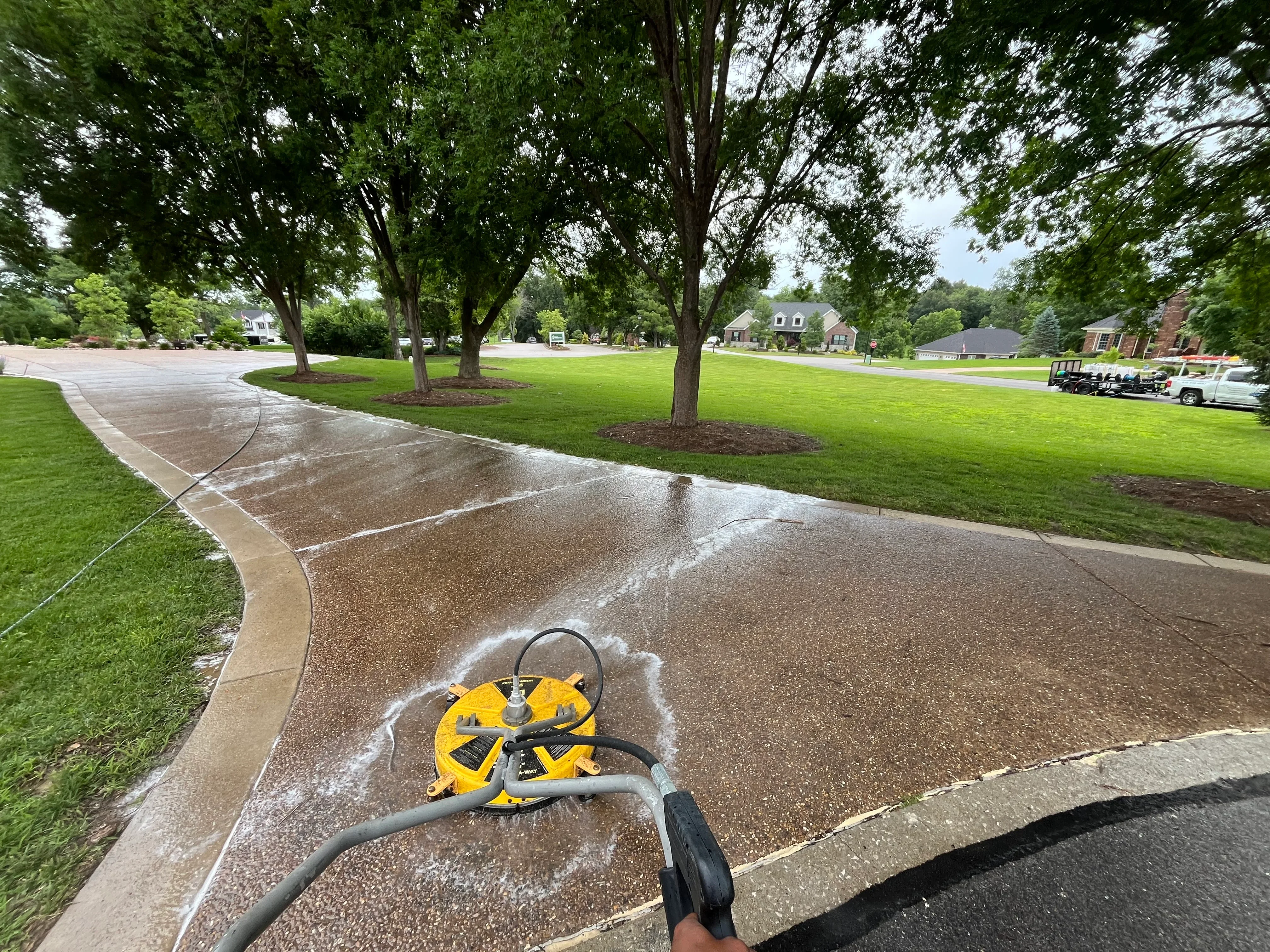 Pressure washer cleaning concrete driveway with yellow equipment visible during active cleaning process