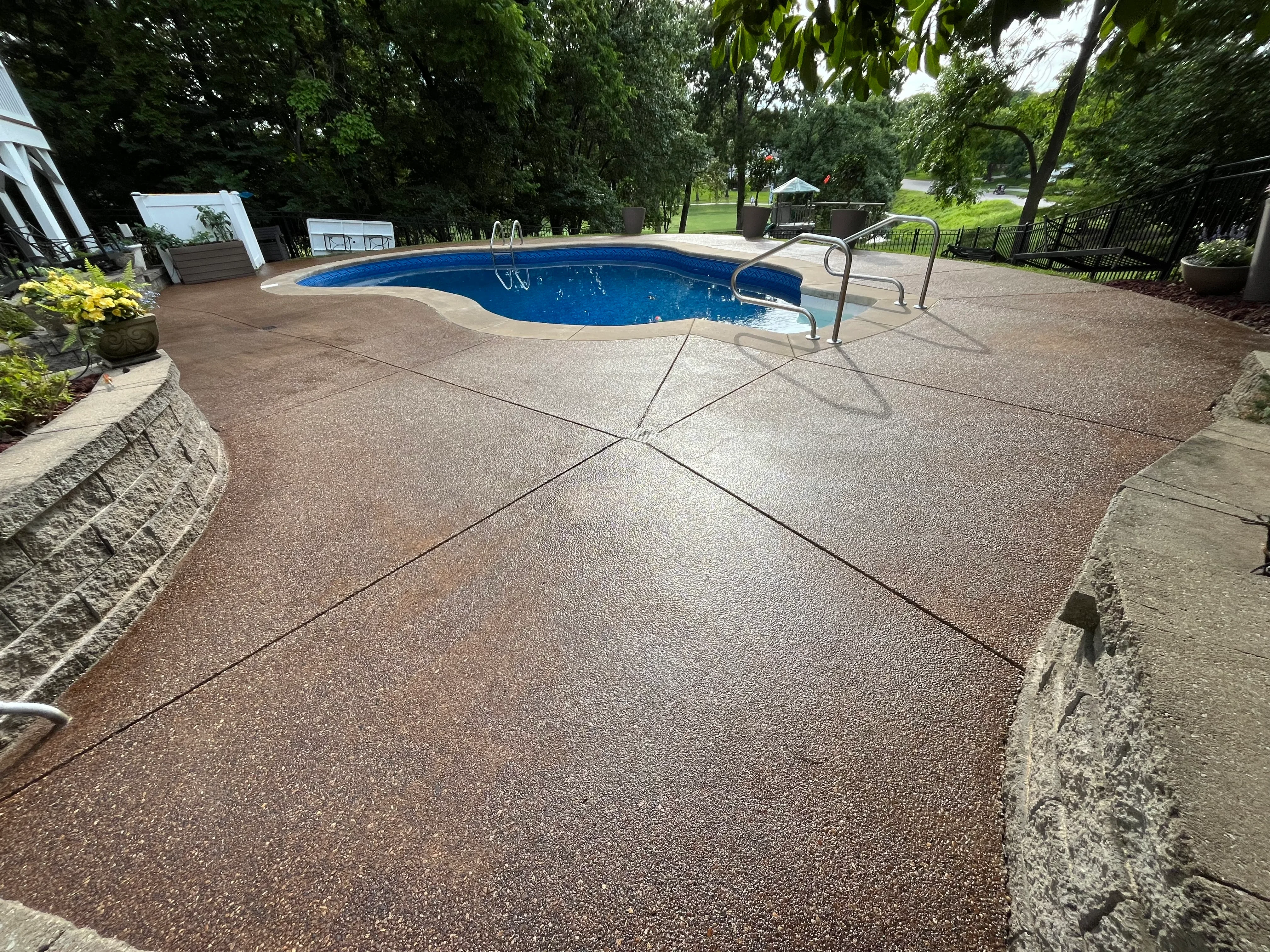 Clean concrete pool deck surrounding blue in-ground pool with metal railings