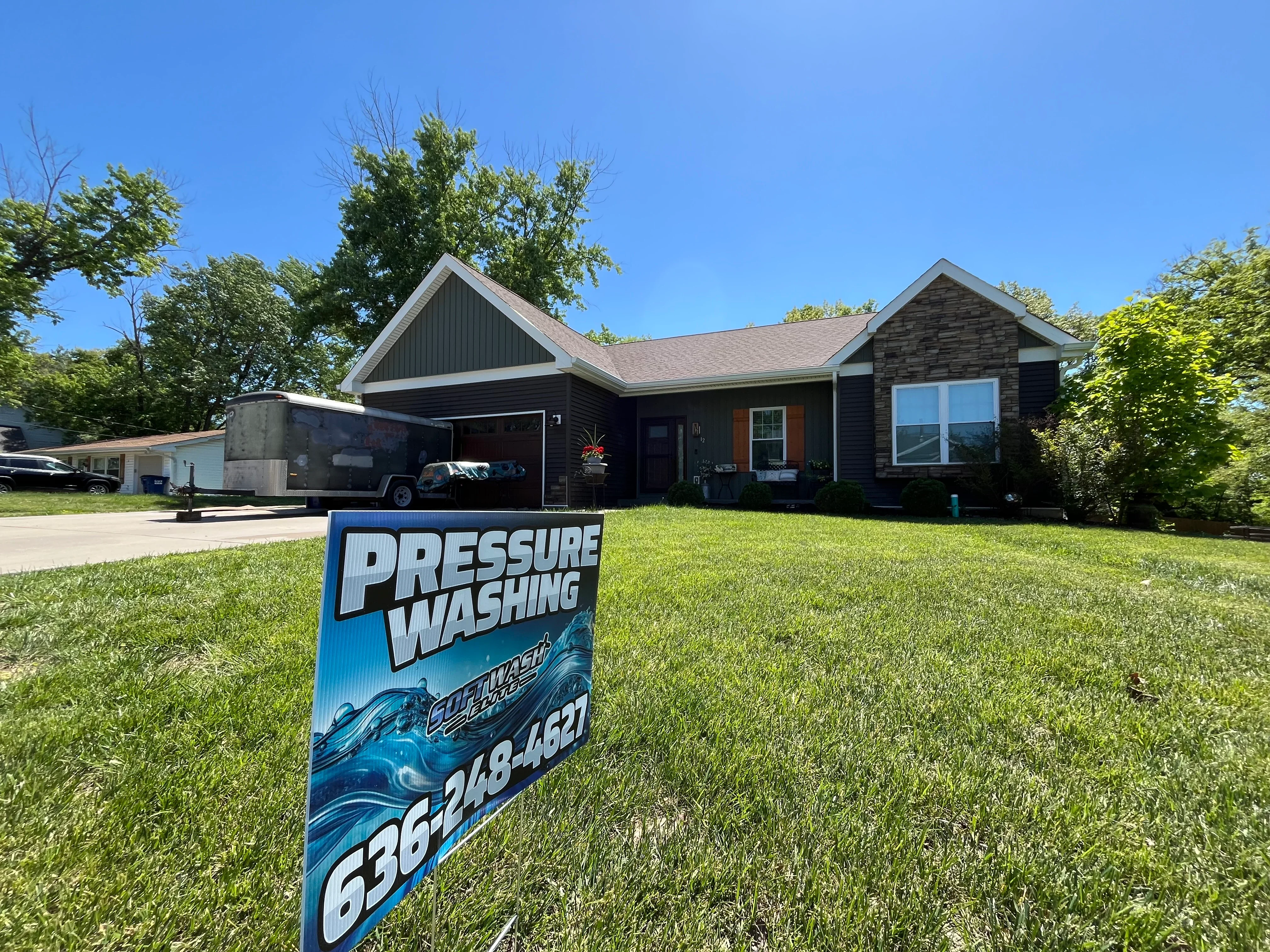 Dark-sided residential home with pressure washing service sign in front yard