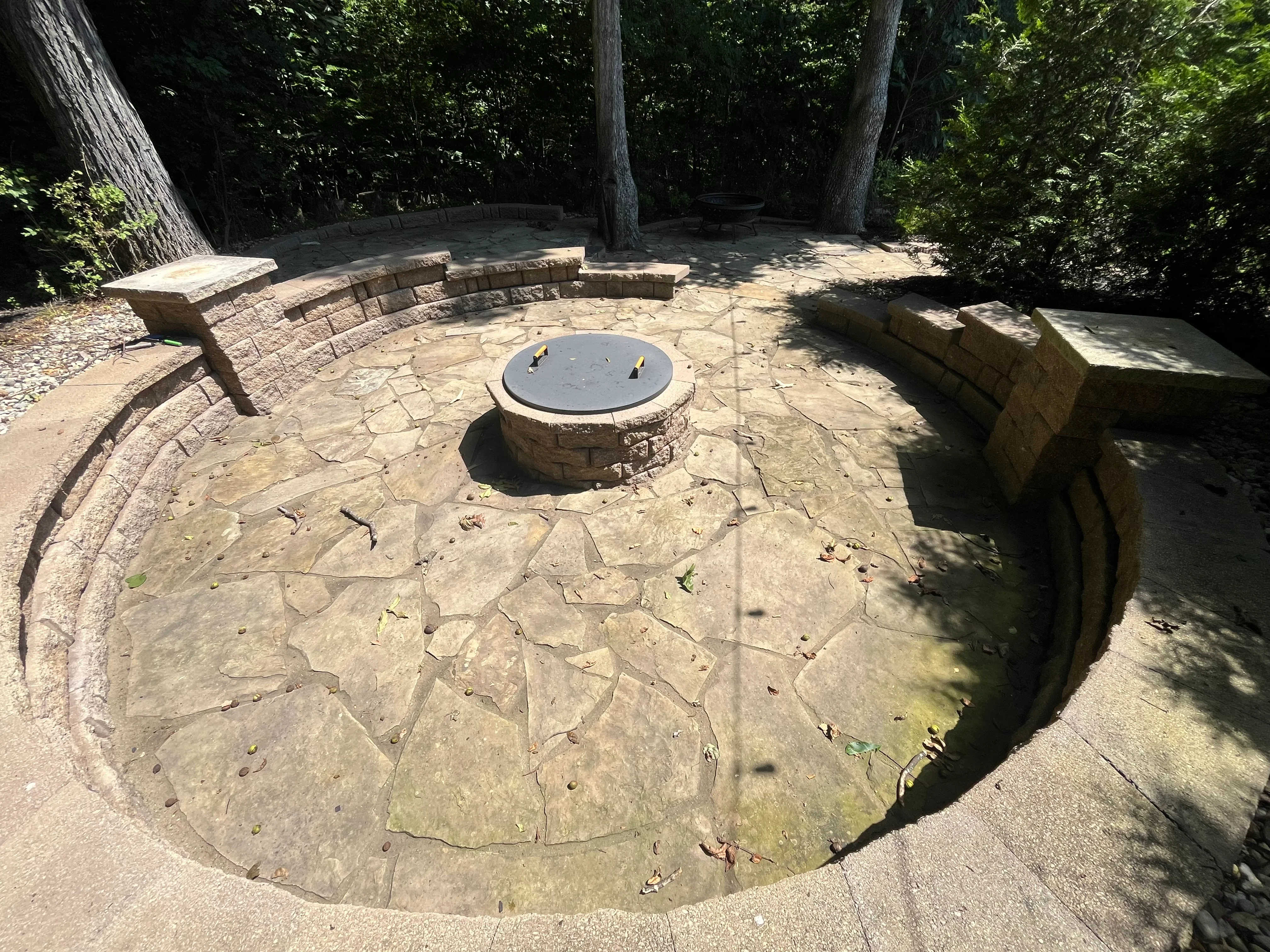 Cleaned stamped concrete patio with central fire pit and curved stone seating walls in wooded area