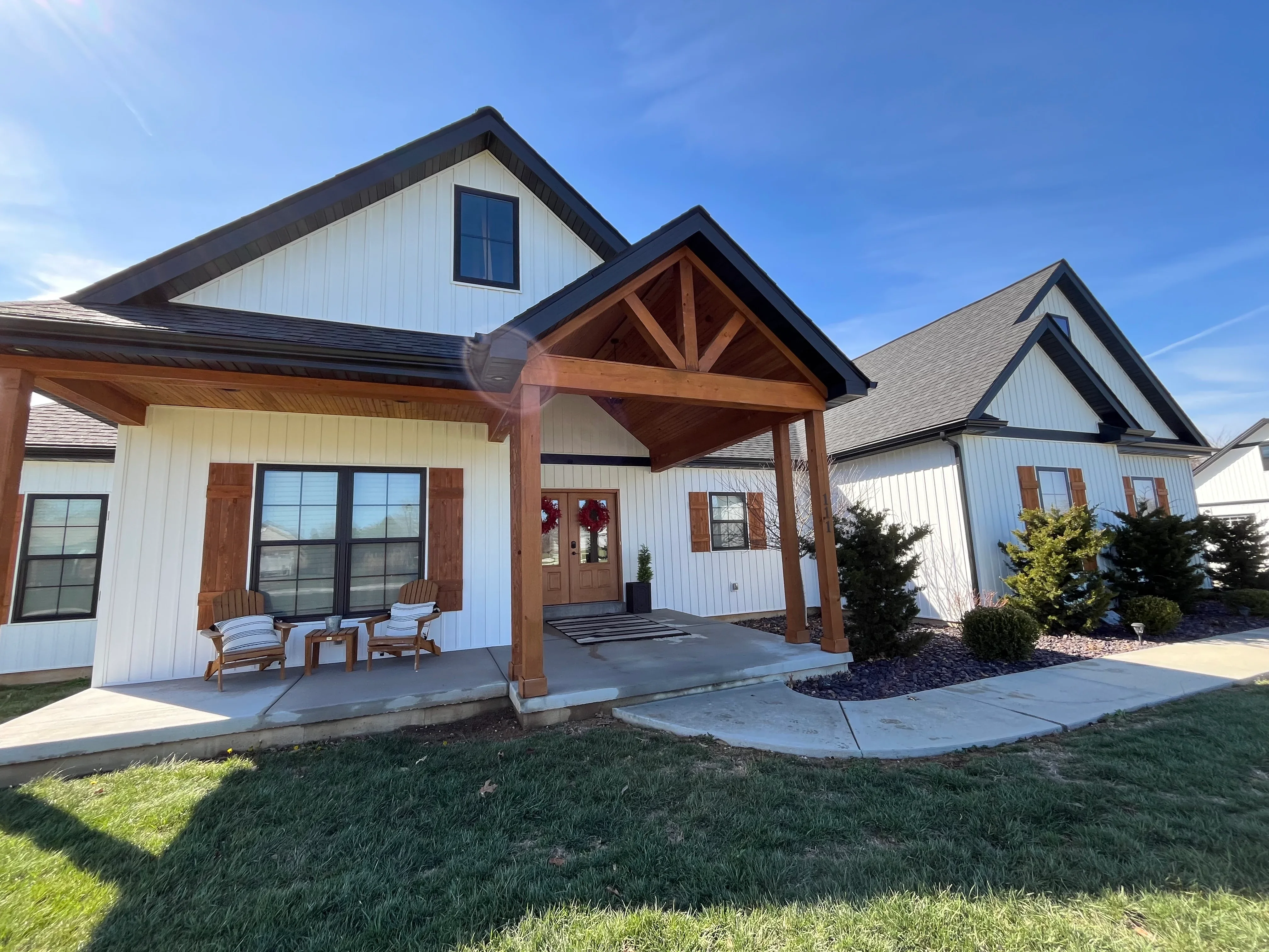 Clean white farmhouse with dark roof and wood pergola after professional pressure washing