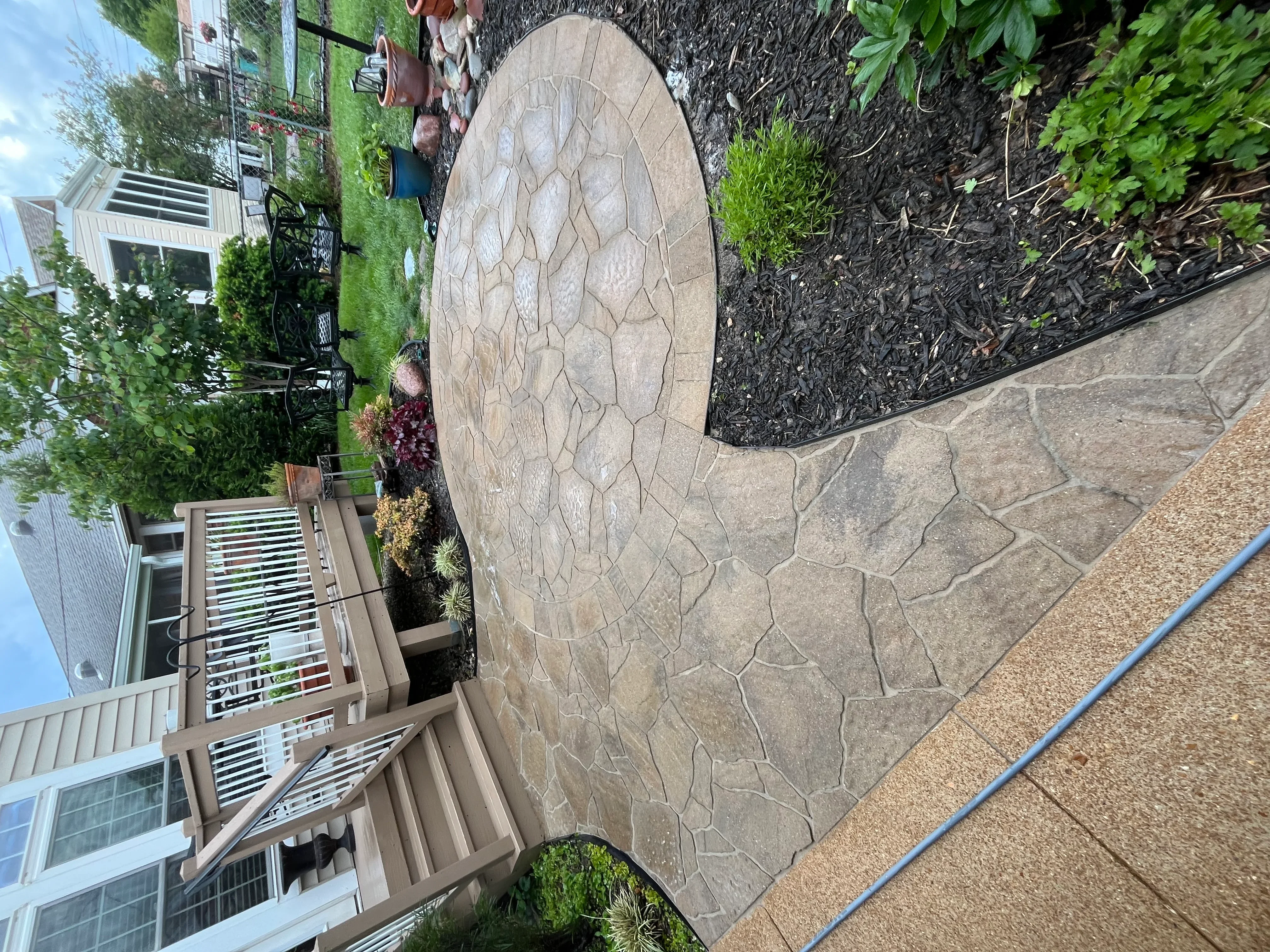 Clean stamped concrete patio with stone pattern design adjacent to landscaped garden beds