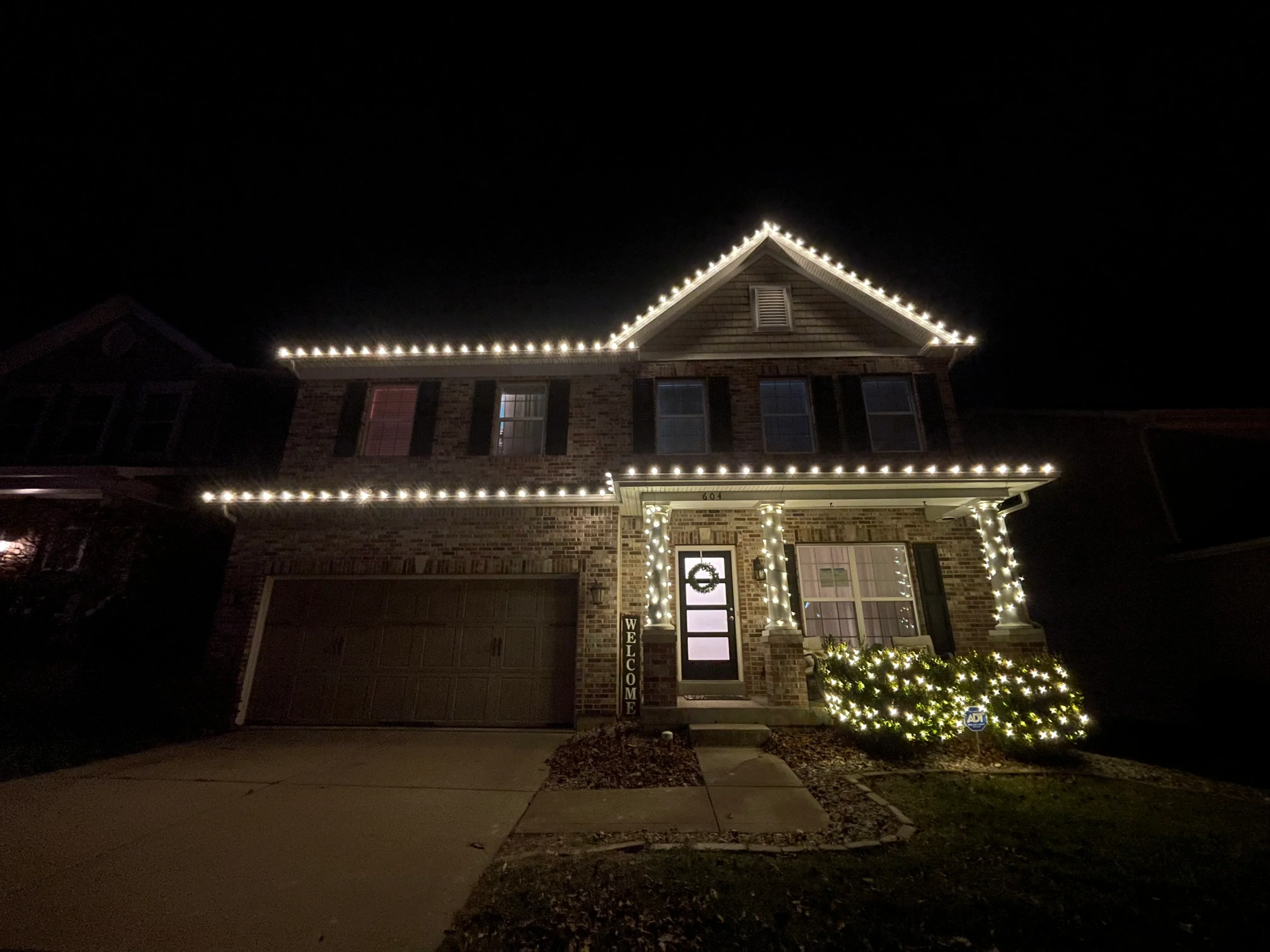 Two-story brick home at night with warm white LED lights outlining roofline and porch