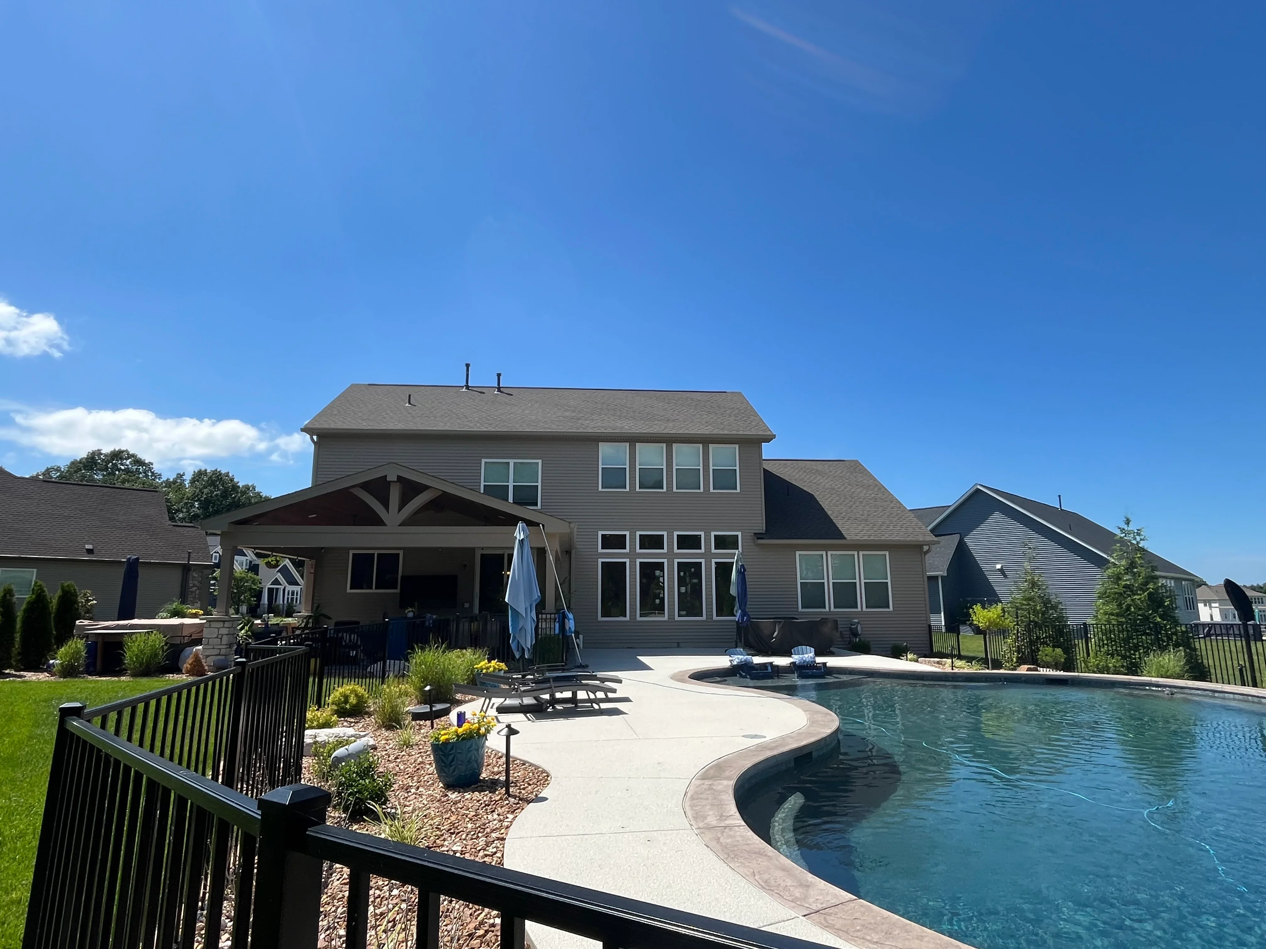 Clean concrete pool deck with curved edges, black fencing, and landscaping around residential pool