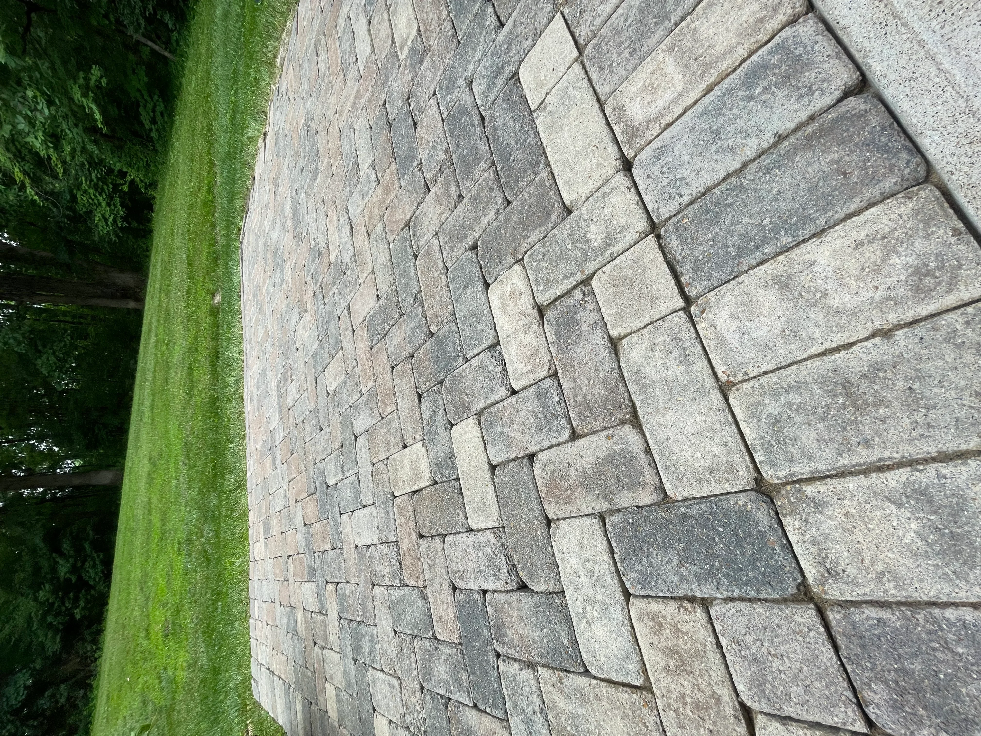 Clean gray and tan paver patio with herringbone pattern and manicured grass border