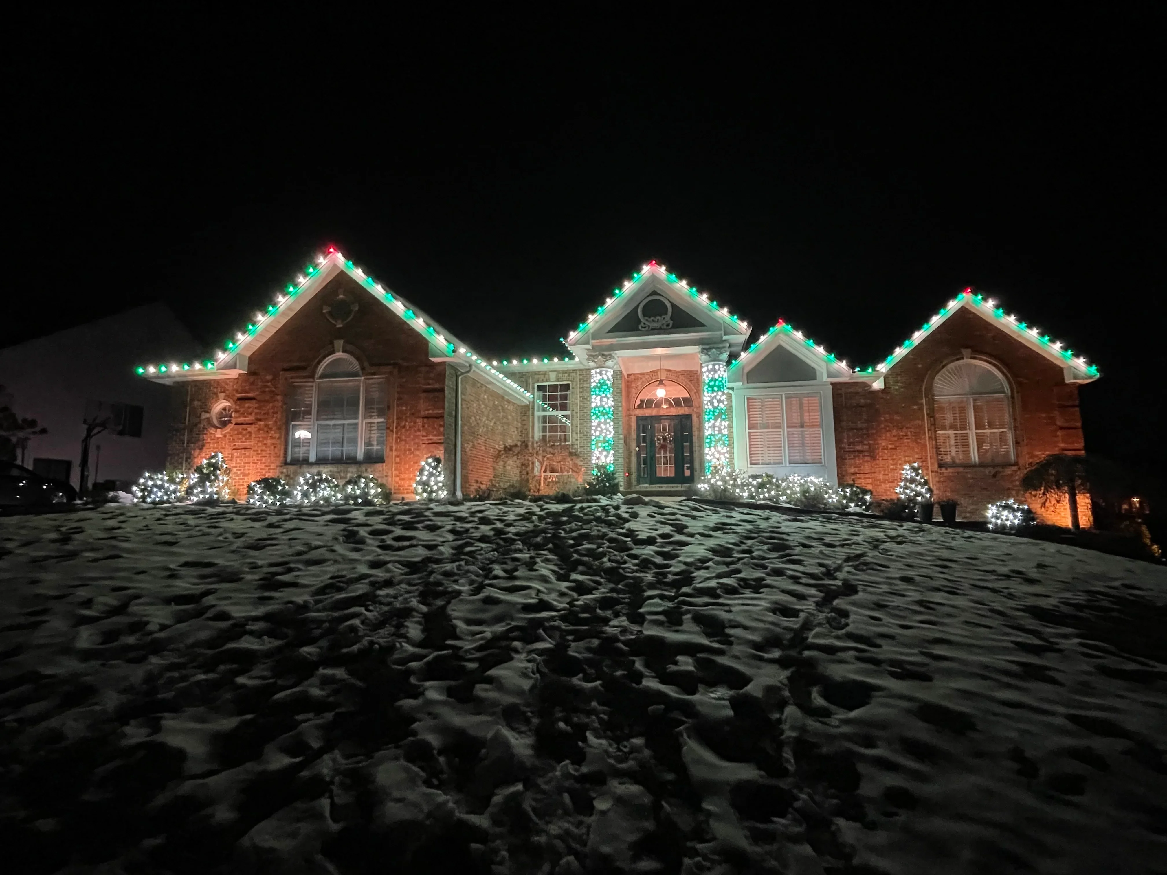 Brick home at night with red uplighting and green-red LED rope lights on roofline