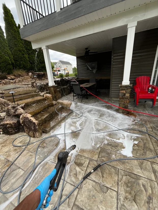 Soft washing stamped concrete patio under covered deck with pressure equipment in use