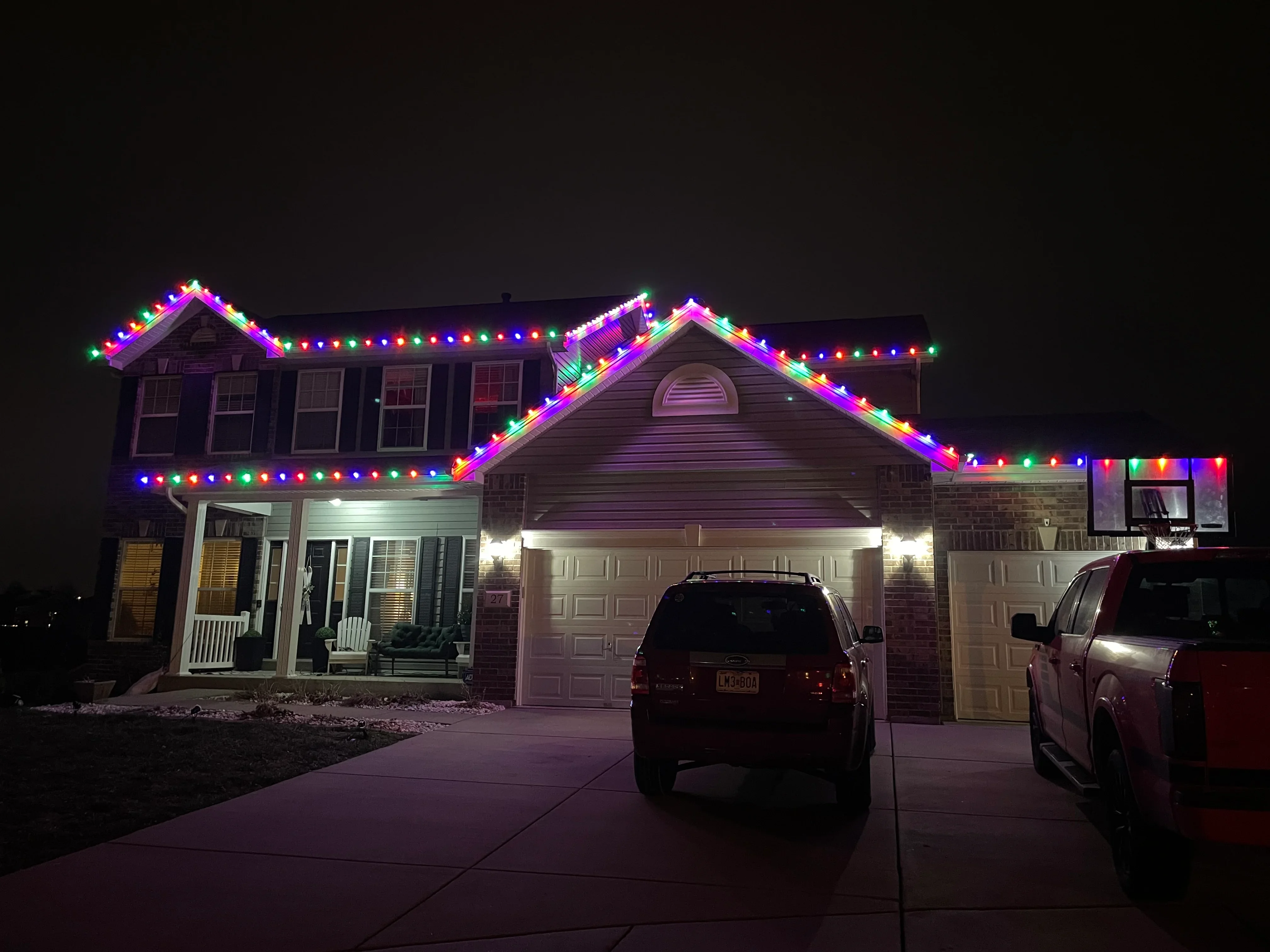 Two-story home with multicolor LED holiday lights installed along roofline and gables at night