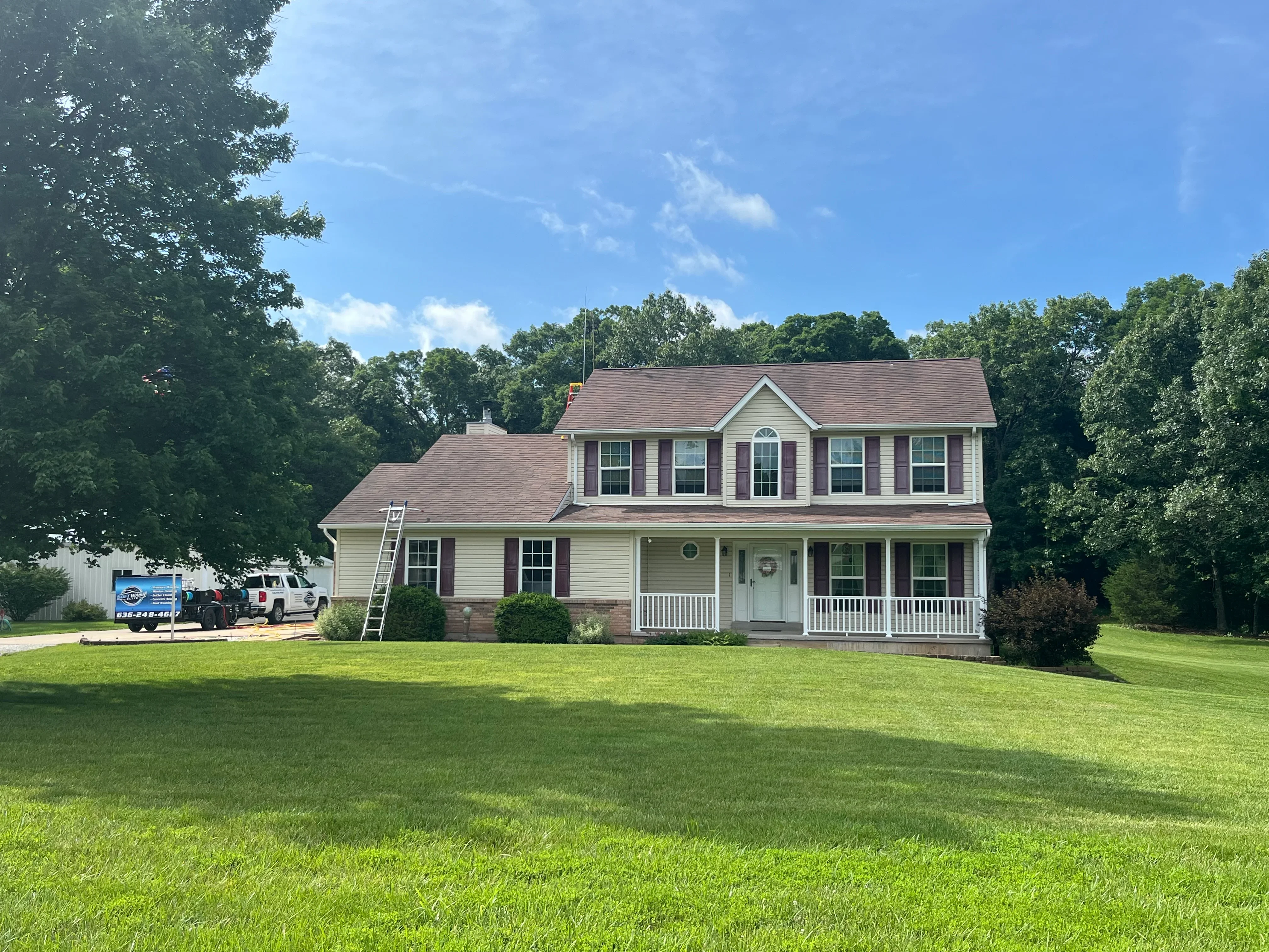 Two-story colonial home with clean vinyl siding, brick base, and white trim after professional pressure washing