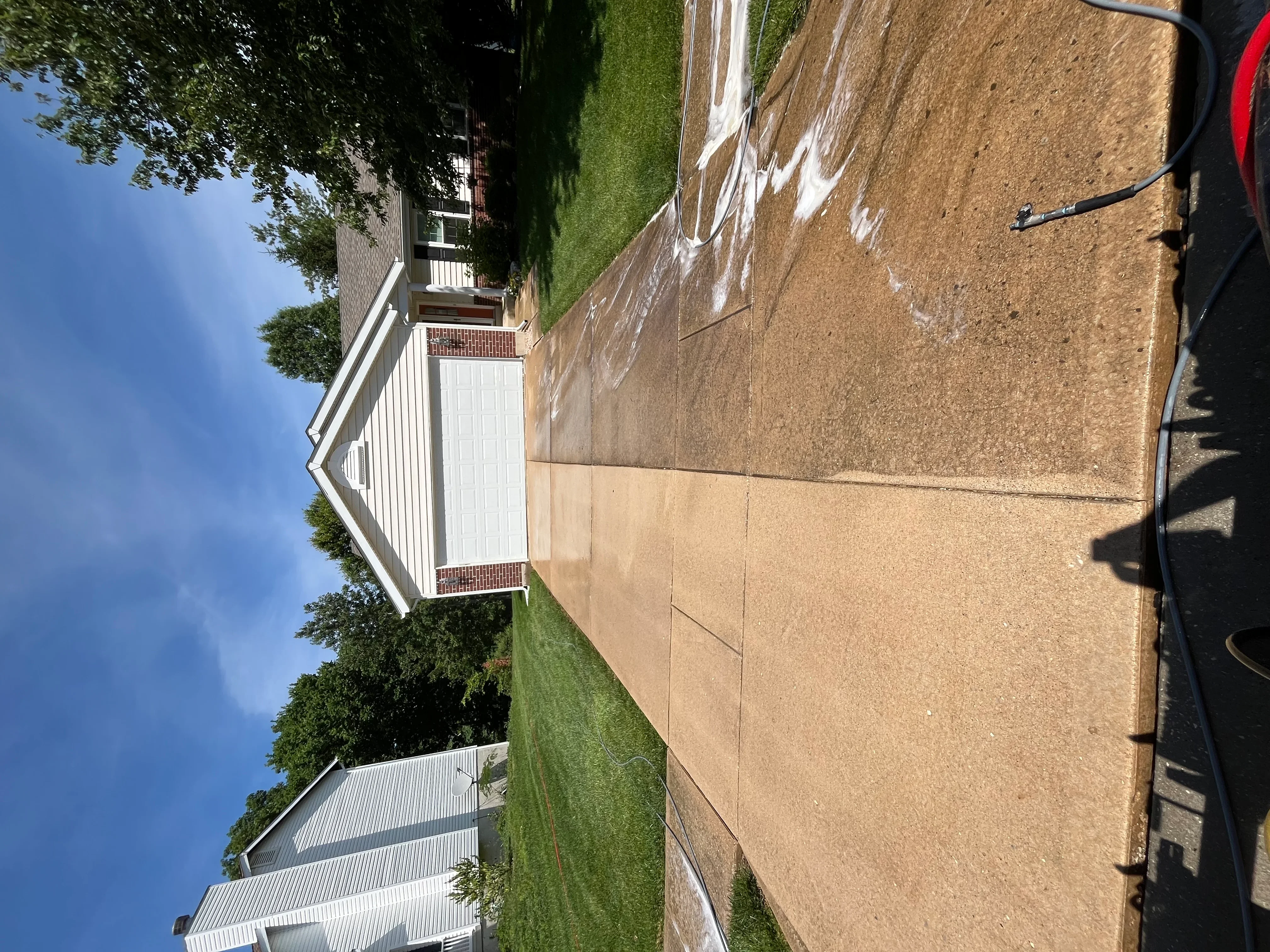 Clean concrete driveway and walkway leading to brick home with white trim