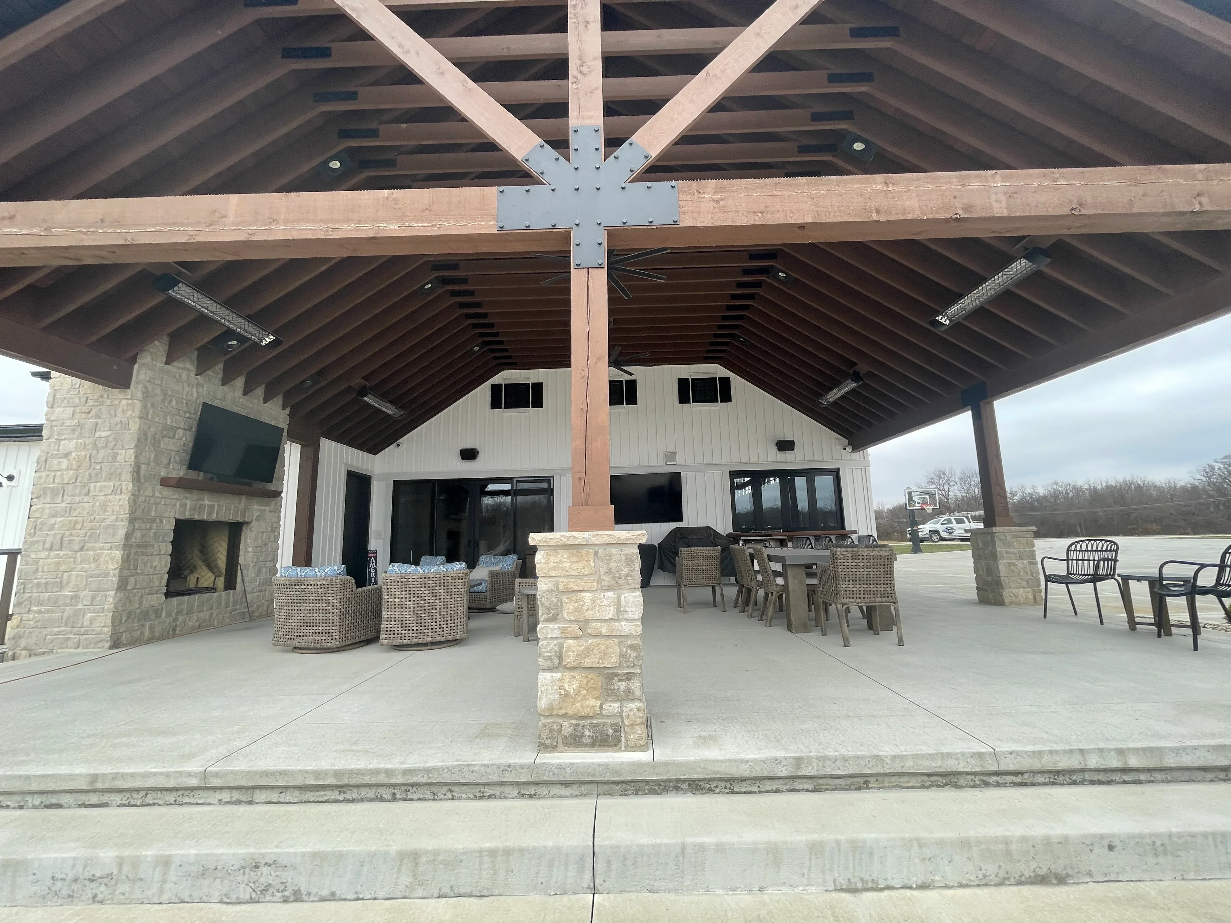 Clean concrete patio with stone pillars under timber pavilion with metal bracing