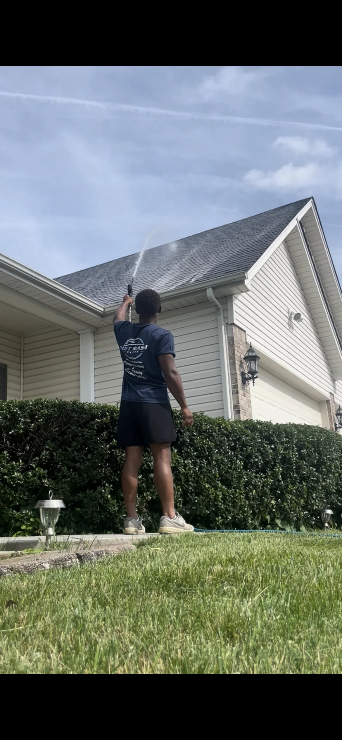 Technician soft washing residential roof with low-pressure equipment on Wentzville home