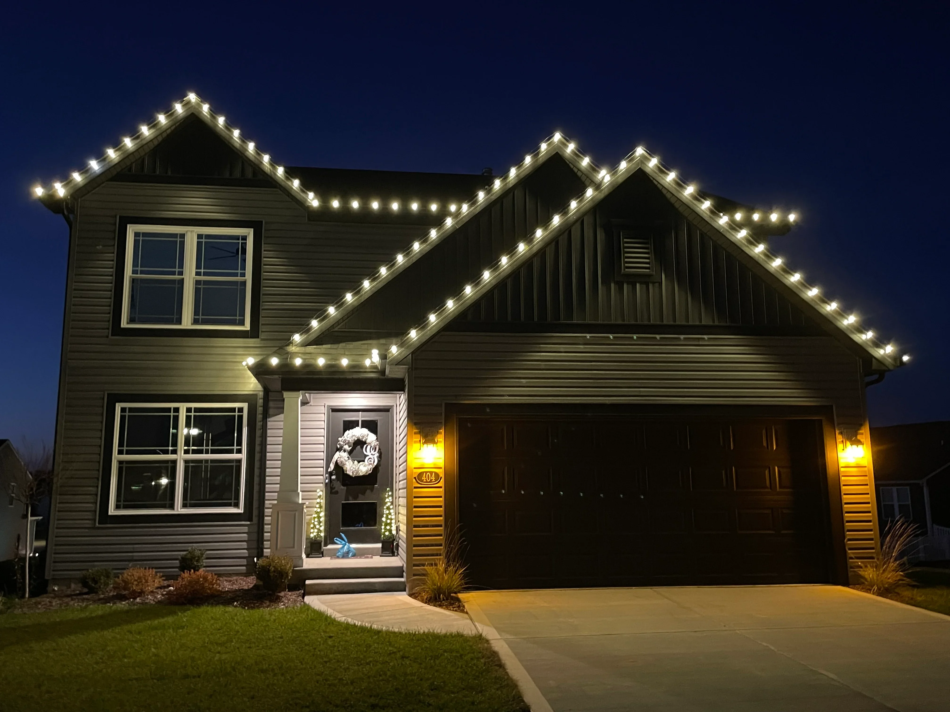 Two-story home with warm white LED lights outlining rooflines and gables at dusk