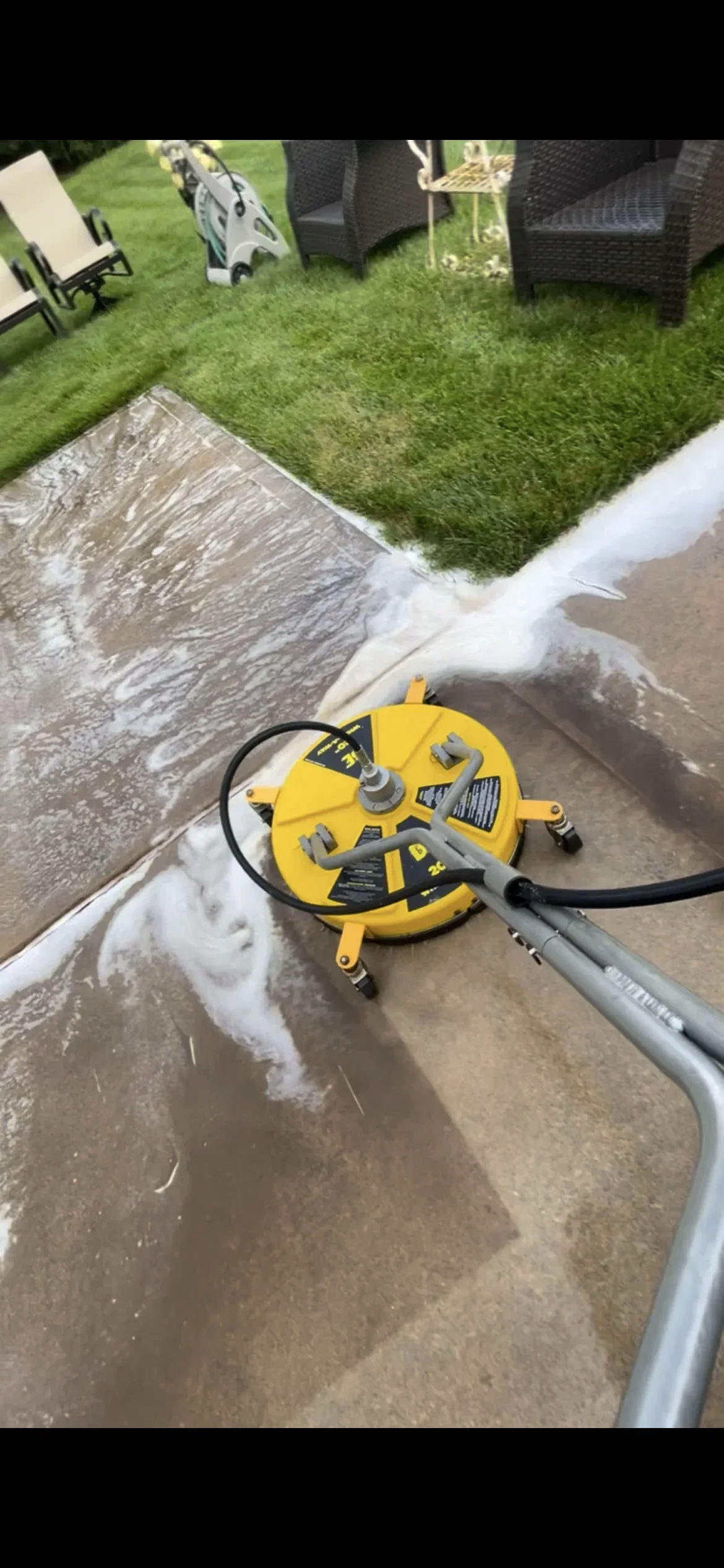 Yellow pressure washer on wet concrete patio with foam cleaning solution applied