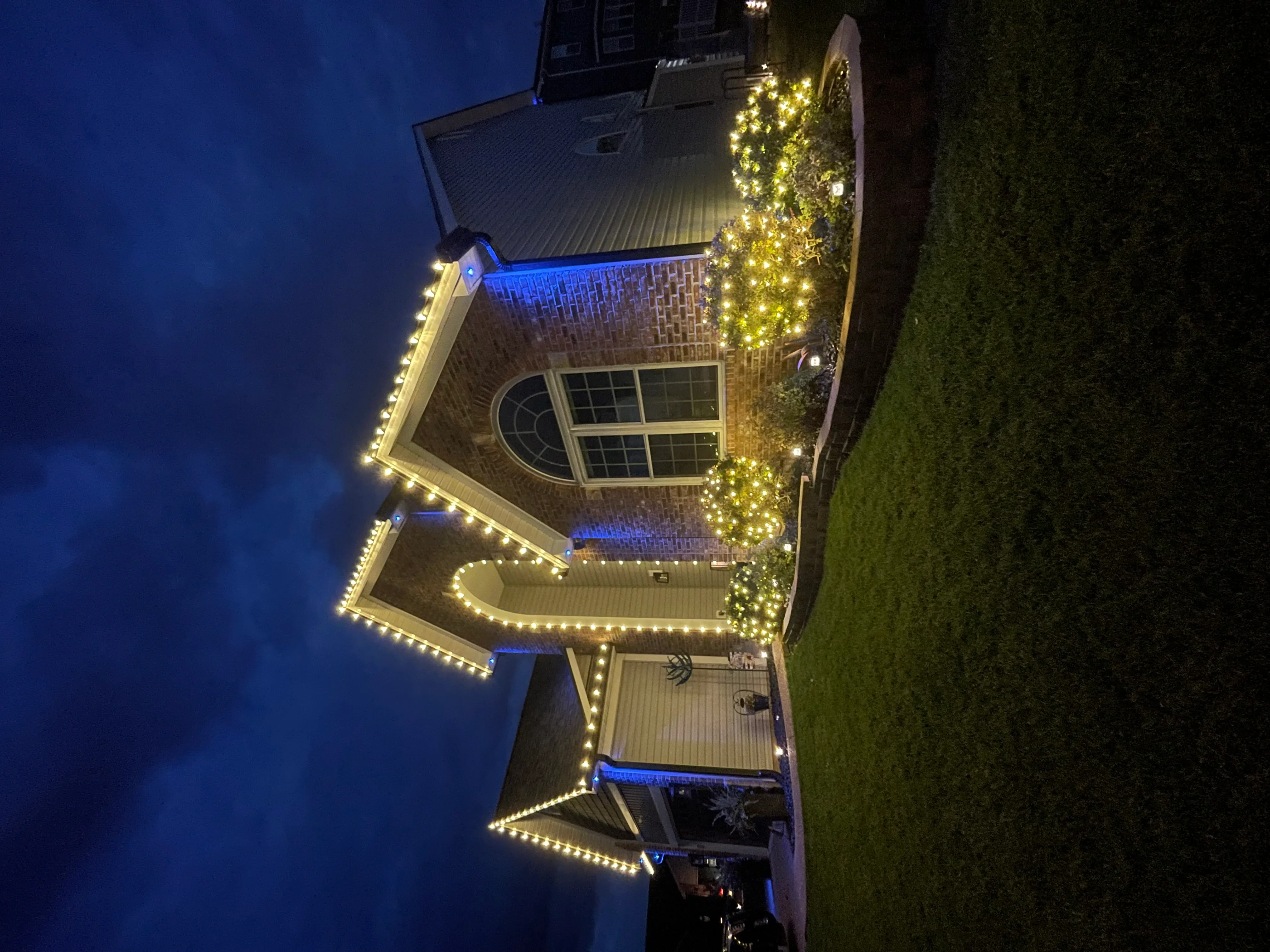 Brick home at night with warm white LED lights outlining roofline and blue accent lighting on facade
