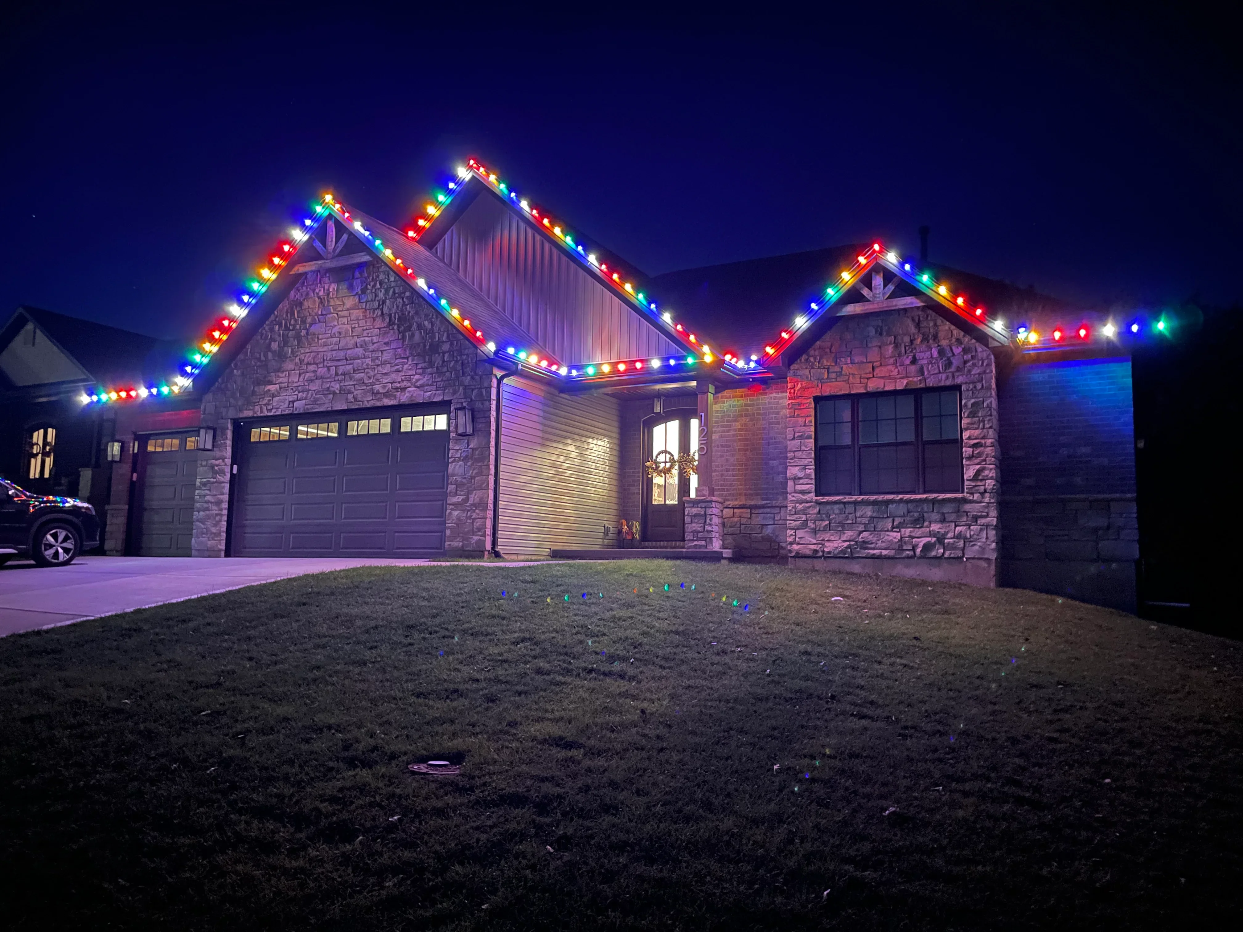 Stone home at night with colorful LED holiday lights installed along roofline and gables