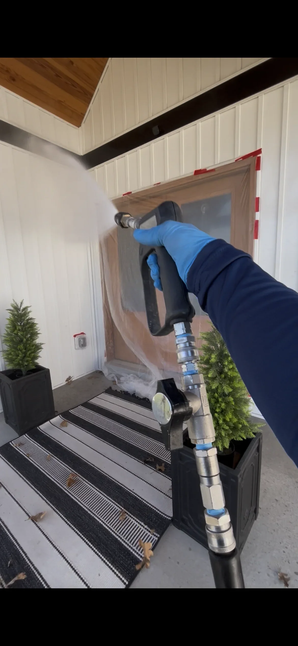 Technician performing soft wash cleaning on residential entryway with white metal siding