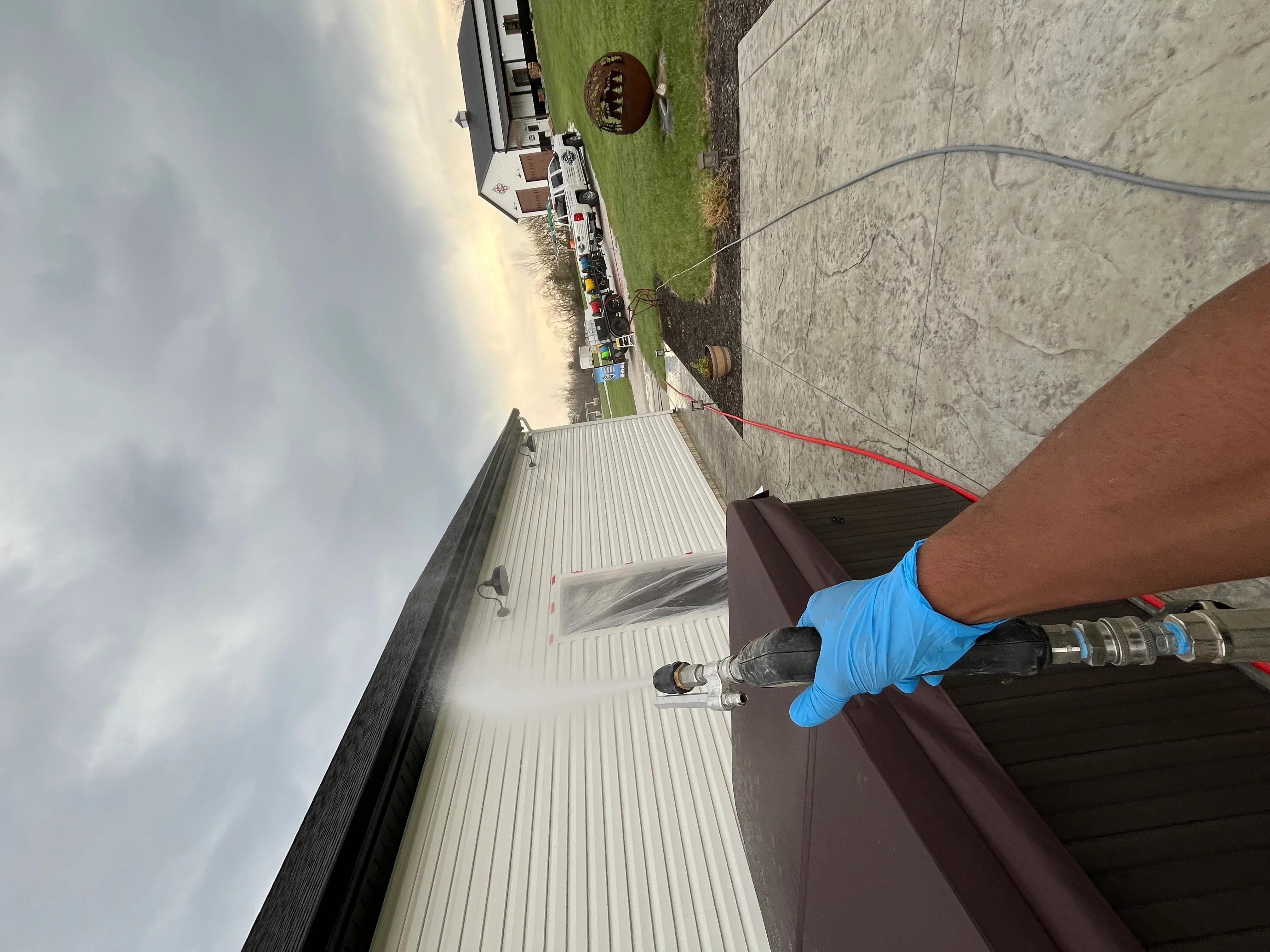 Technician in blue gloves performing soft wash cleaning on residential roof and gutter system
