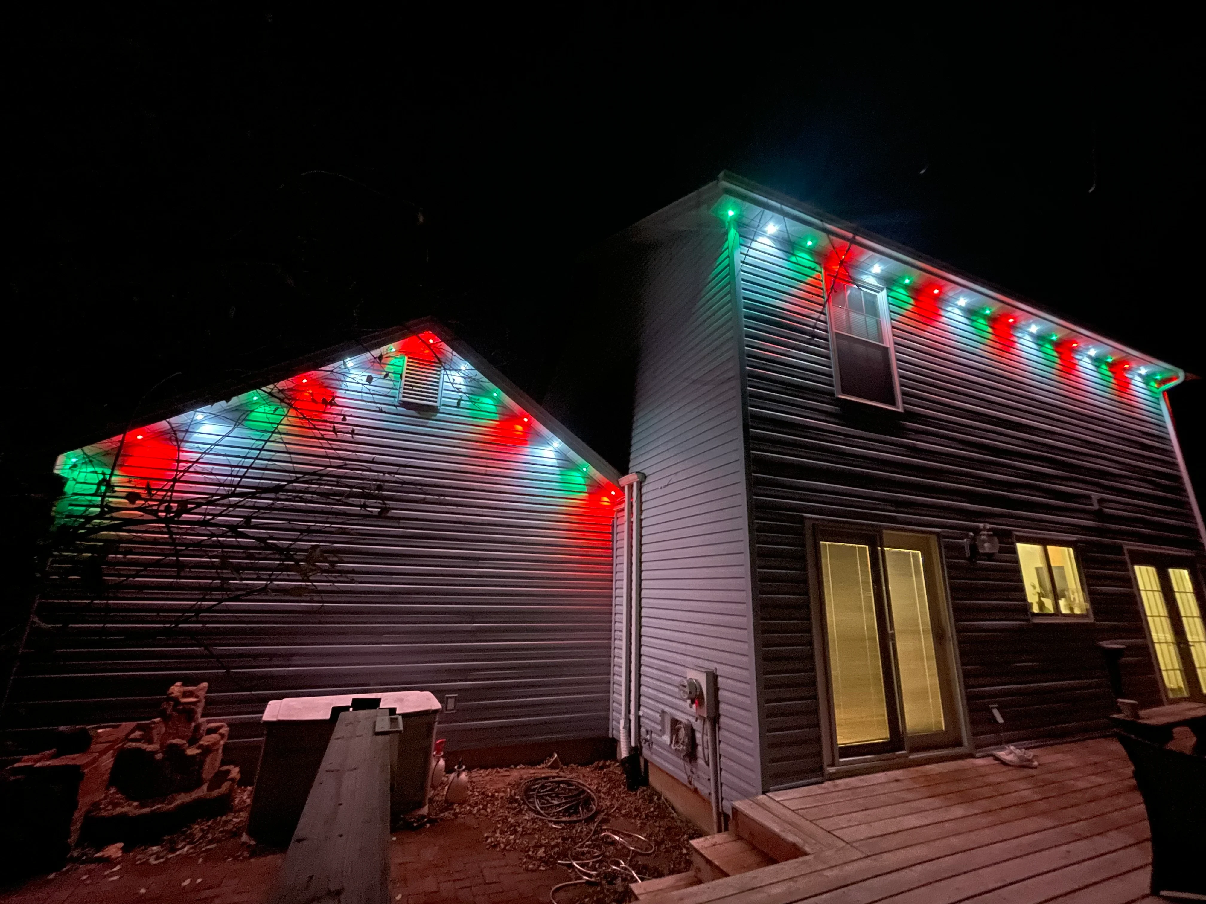 Residential home with red, green, and white LED holiday lights installed on roofline at night
