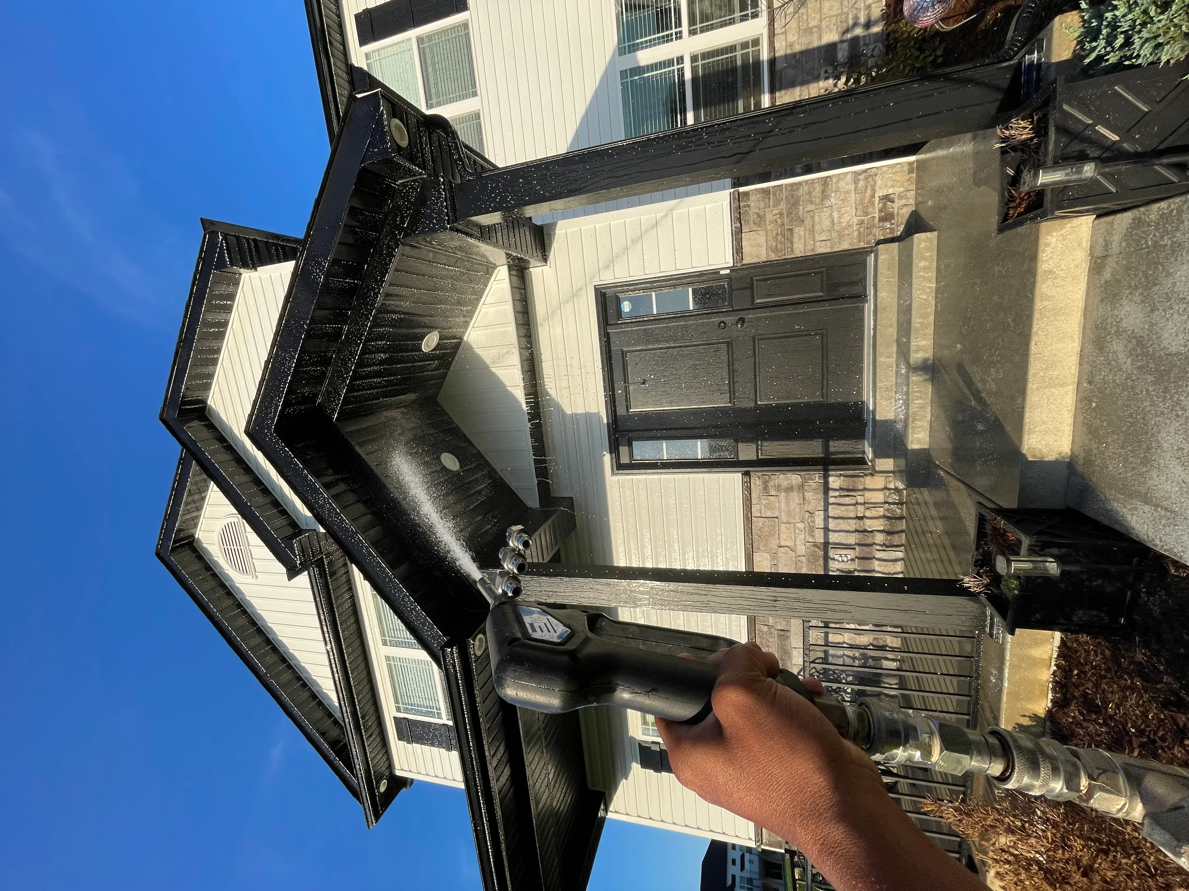 Technician performing soft wash cleaning on residential home exterior with metal siding